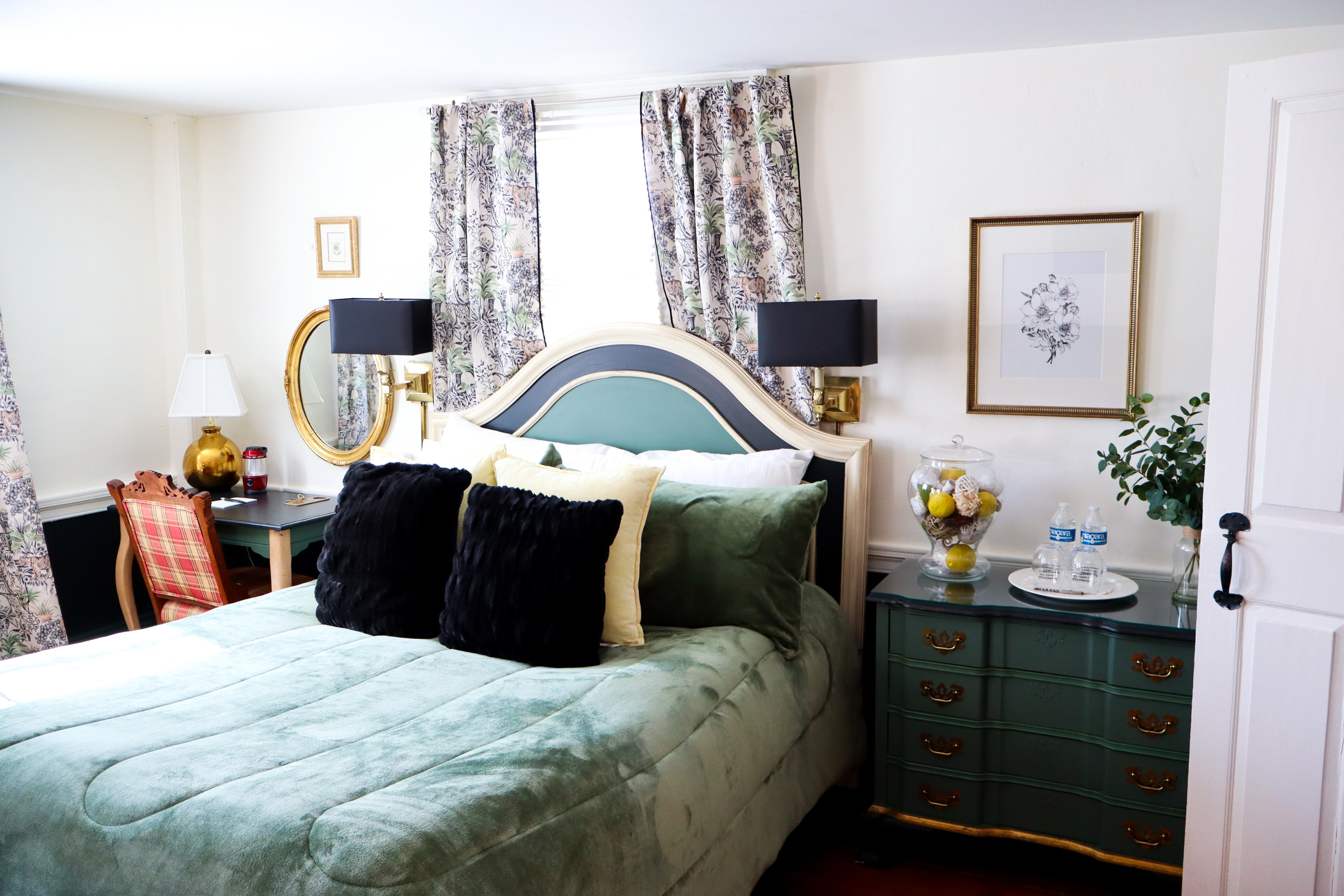 A cozy corner featuring a lit fireplace, a small writing desk with a lamp, and a comfy upholstered armchair, all against vintage patterned wallpaper.