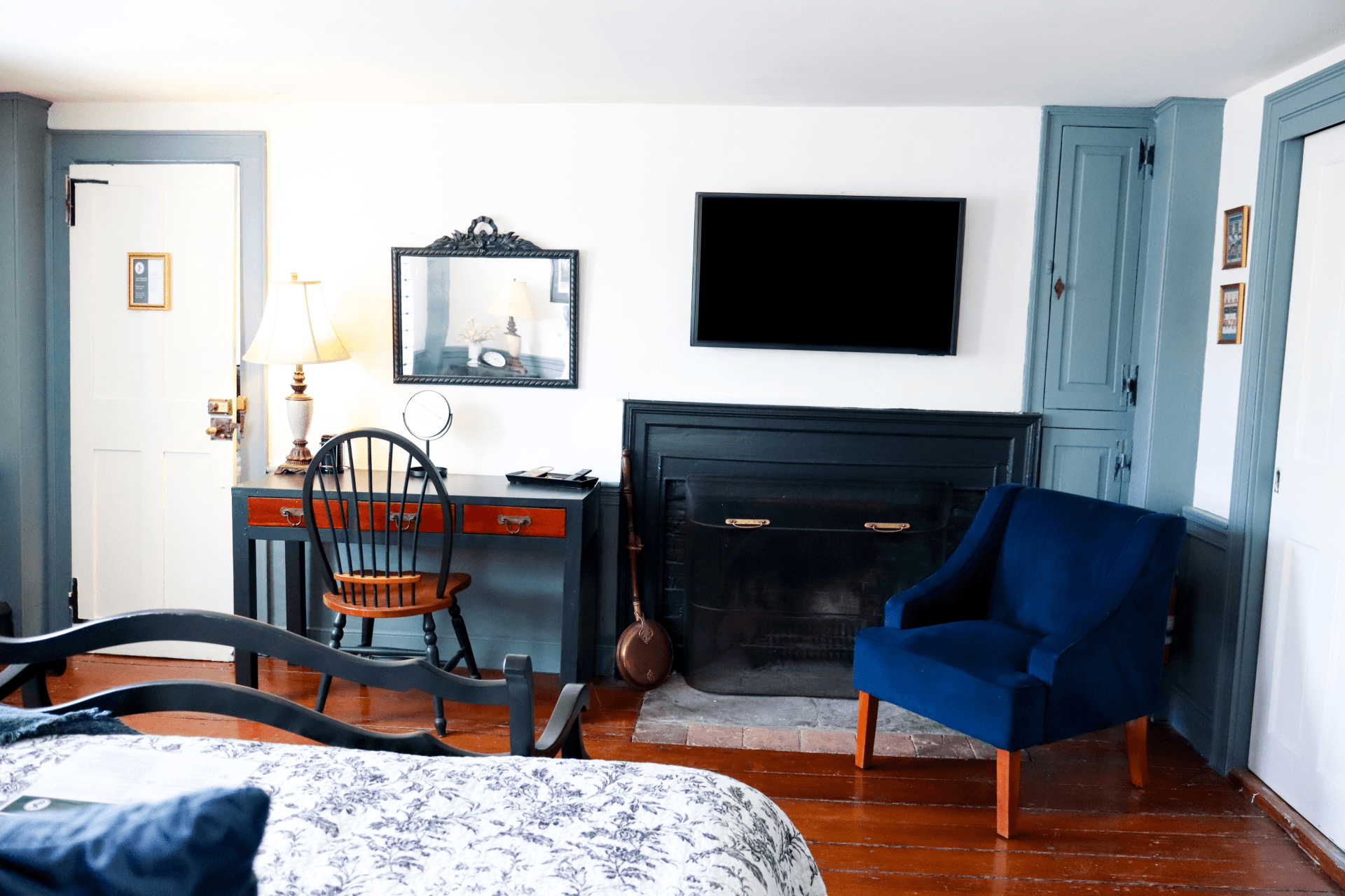 A quaint room featuring delicate floral wallpaper, bright green trim, a small wood writing desk with a lamp, and an open doorway.