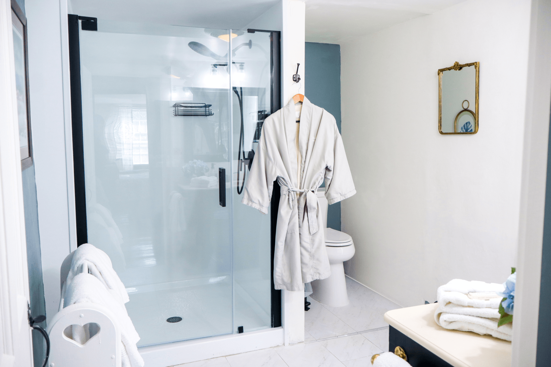A vintage-style pink bathroom featuring a built-in tub, a glass shower stall, and a cozy gray bathrobe hanging on the wall.