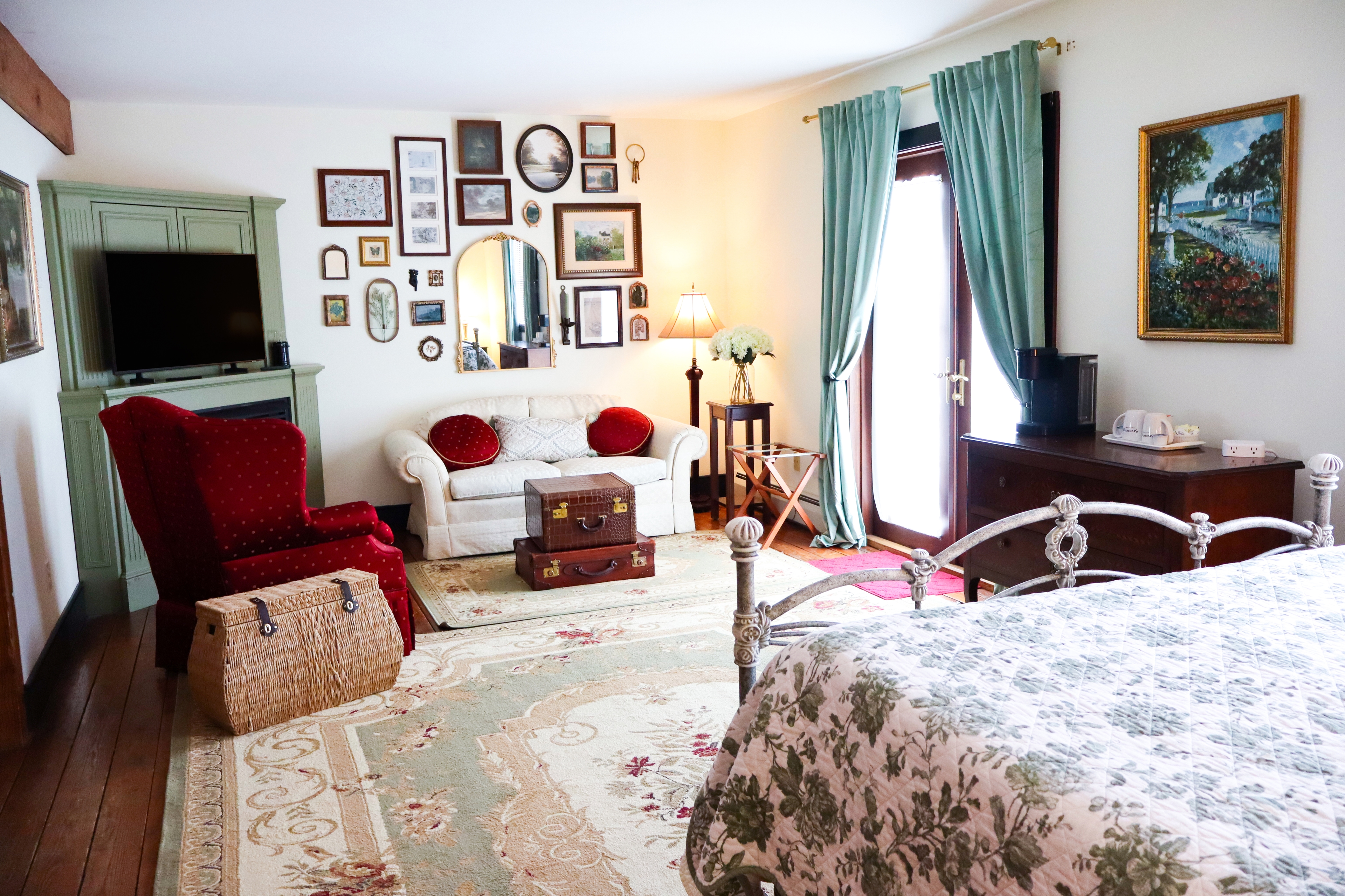 A bright, romantic bedroom with a scrollwork metal bed frame, a light green antique dresser, and a doorway leading to an adjoining room.