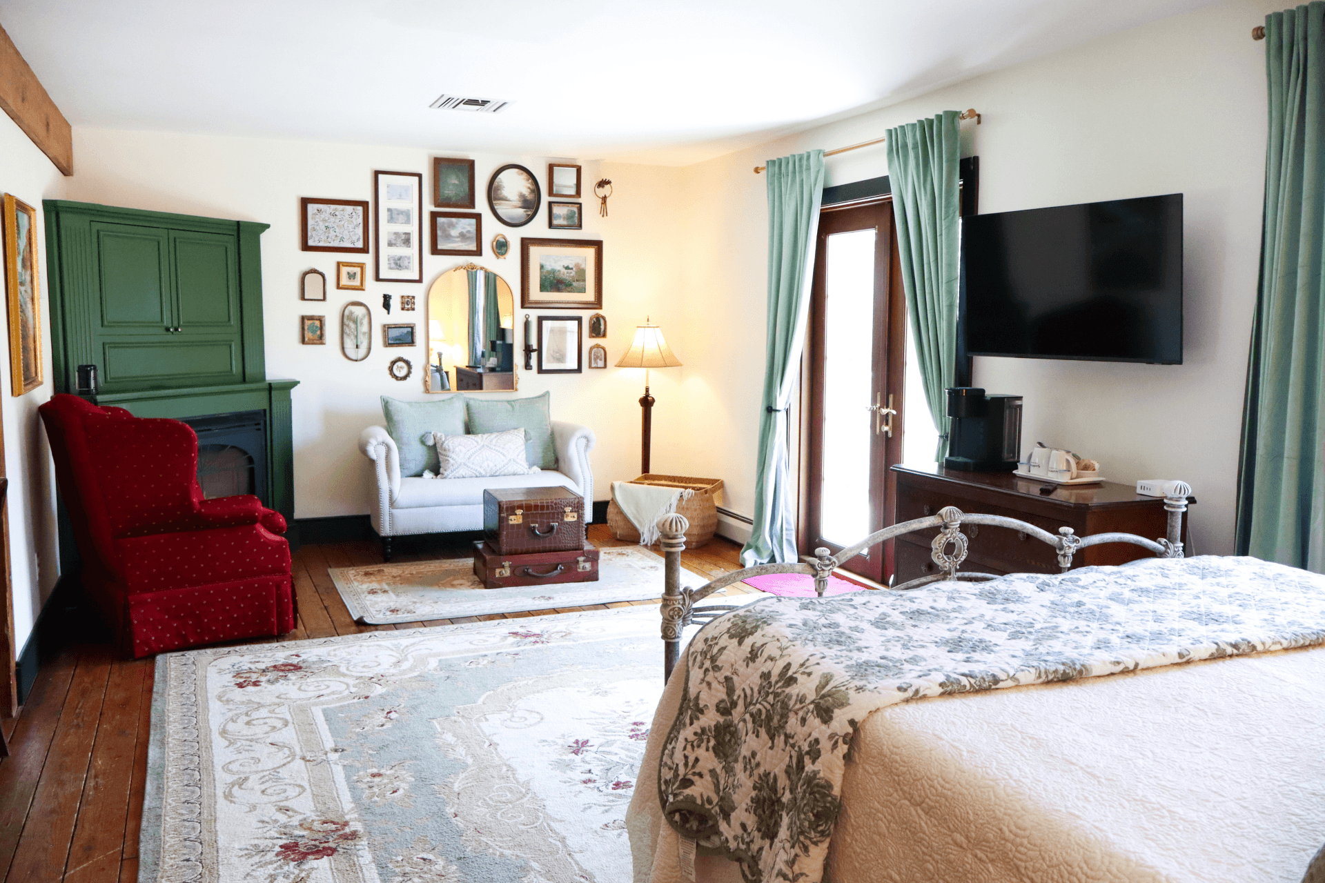A bright, romantic bedroom with a scrollwork metal bed frame, a light green antique dresser, and a doorway leading to an adjoining room.