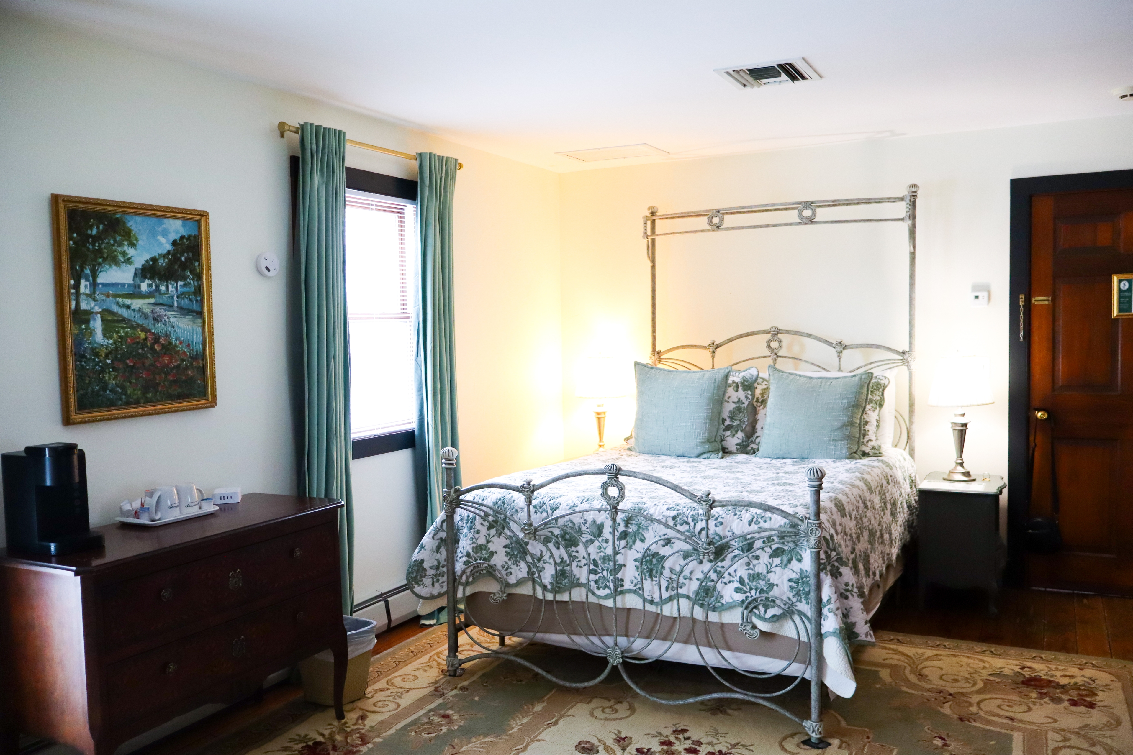 A cozy sitting area featuring a lit fireplace set in a sage-green mantel, a comfortable sofa with pillows, and a small table with flowers.