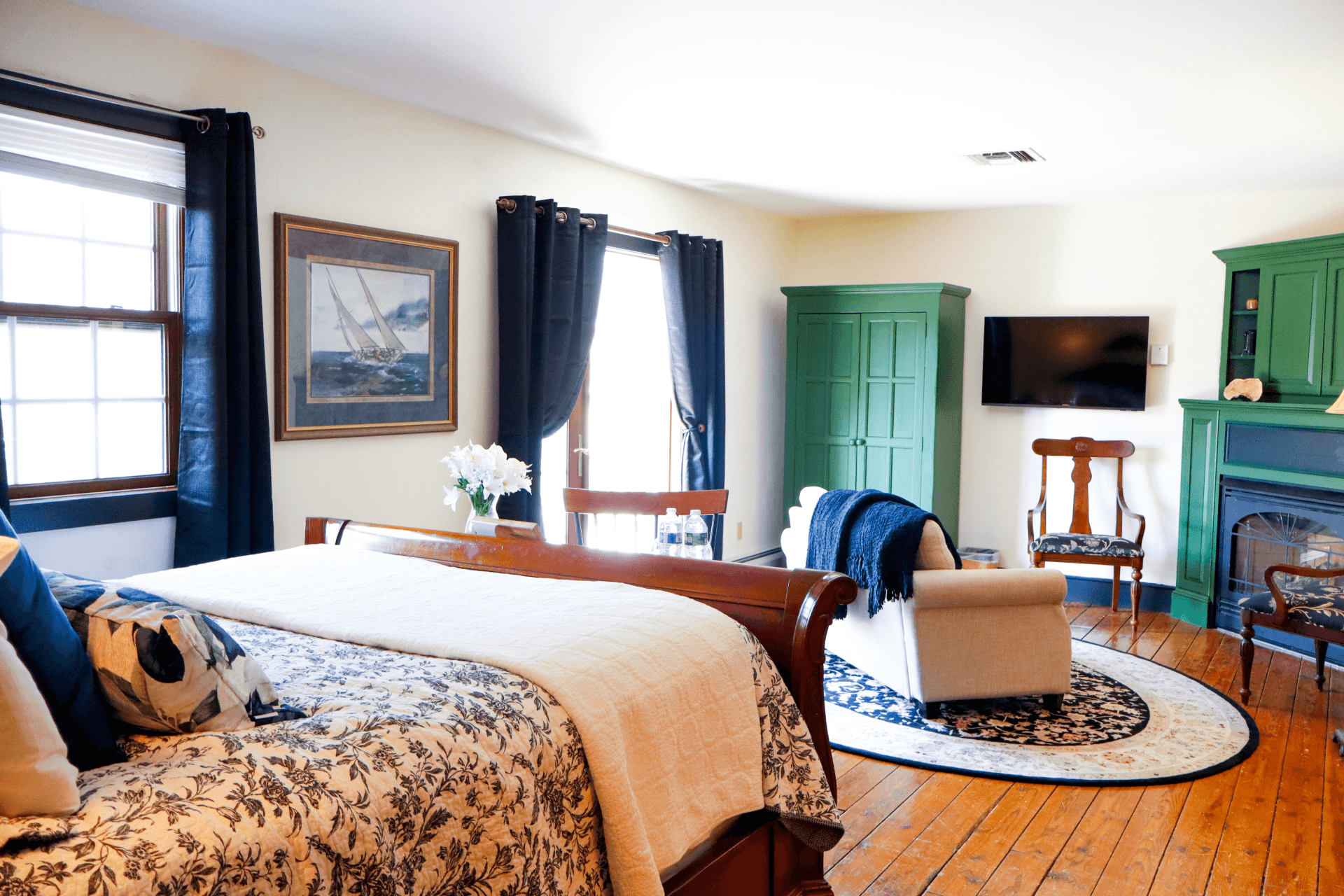 A cozy sitting area with a lit fireplace, a dark blue sofa, a writing desk, and a glass of red wine on a book for a relaxing evening.