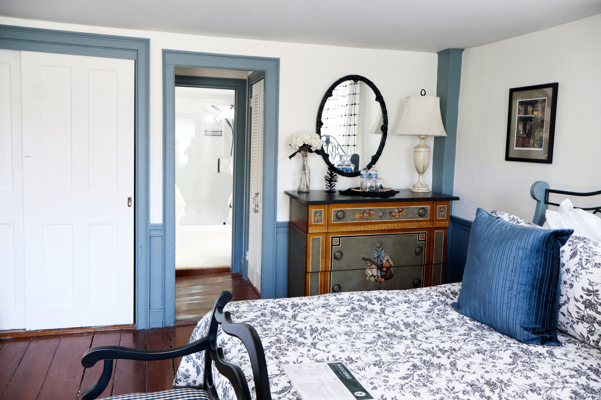 A bright, quaint bathroom featuring a bold green vanity with a white countertop, a mirrored cabinet, and a large window with sheer curtains.