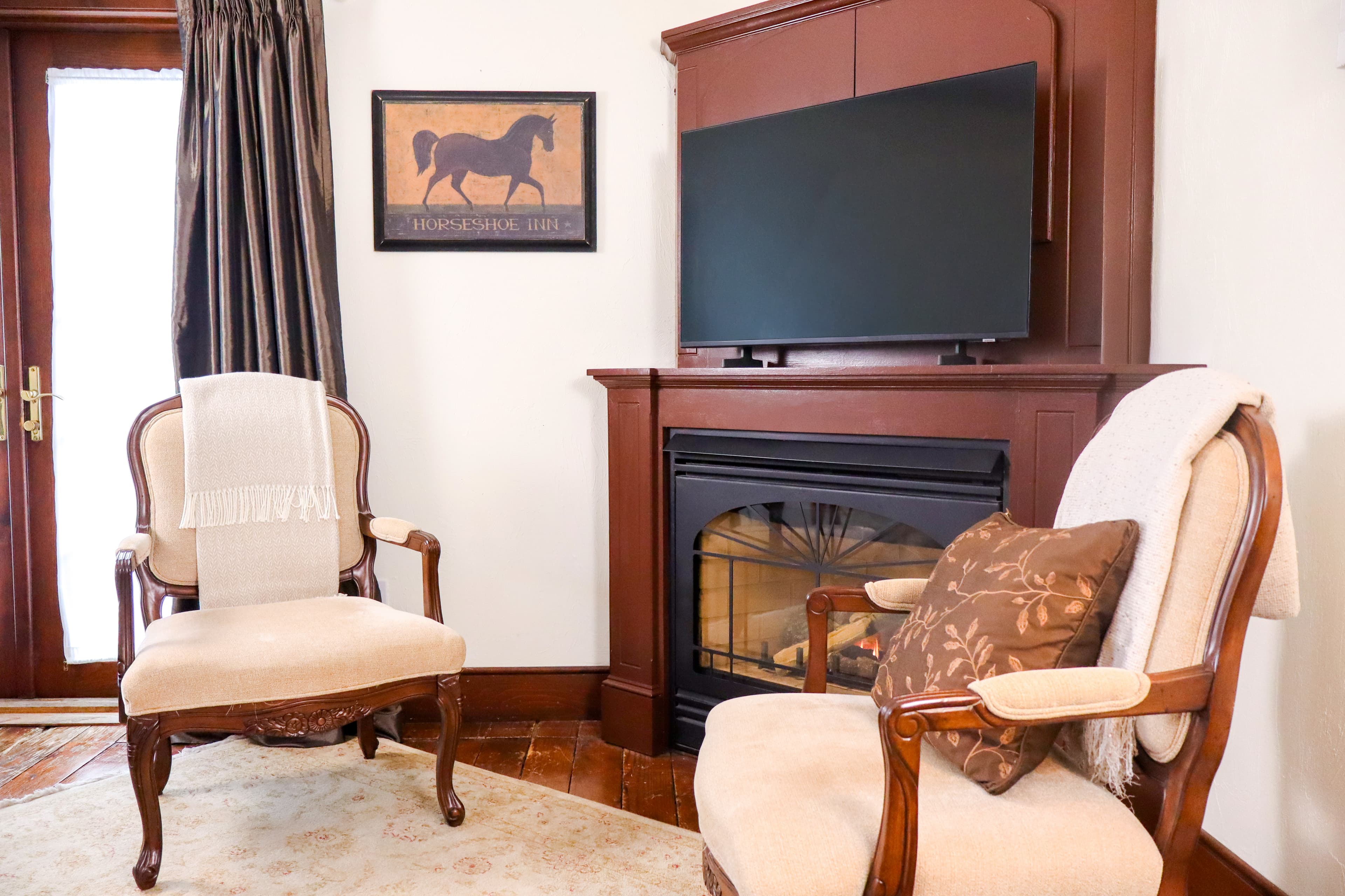 A relaxing bathroom with a deep jetted tub encased in dark wood, a small rose, wine glasses, and a vanity with a framed mirror.