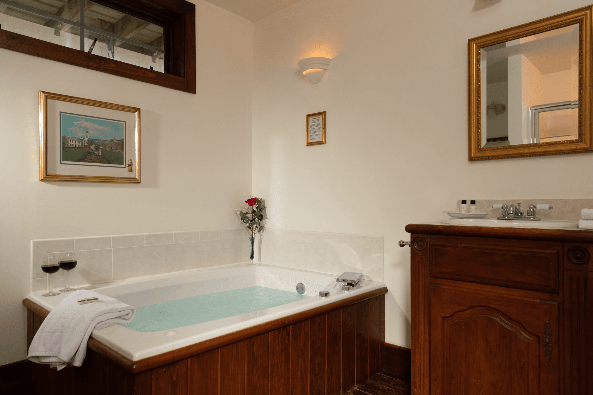 Spa soaking tub with wood panel surround and folded towels in the Briar Rose room bathroom at Stonecroft Country Inn, featuring a romantic bath setup with wine glasses, soft lighting, and elegant antique décor.