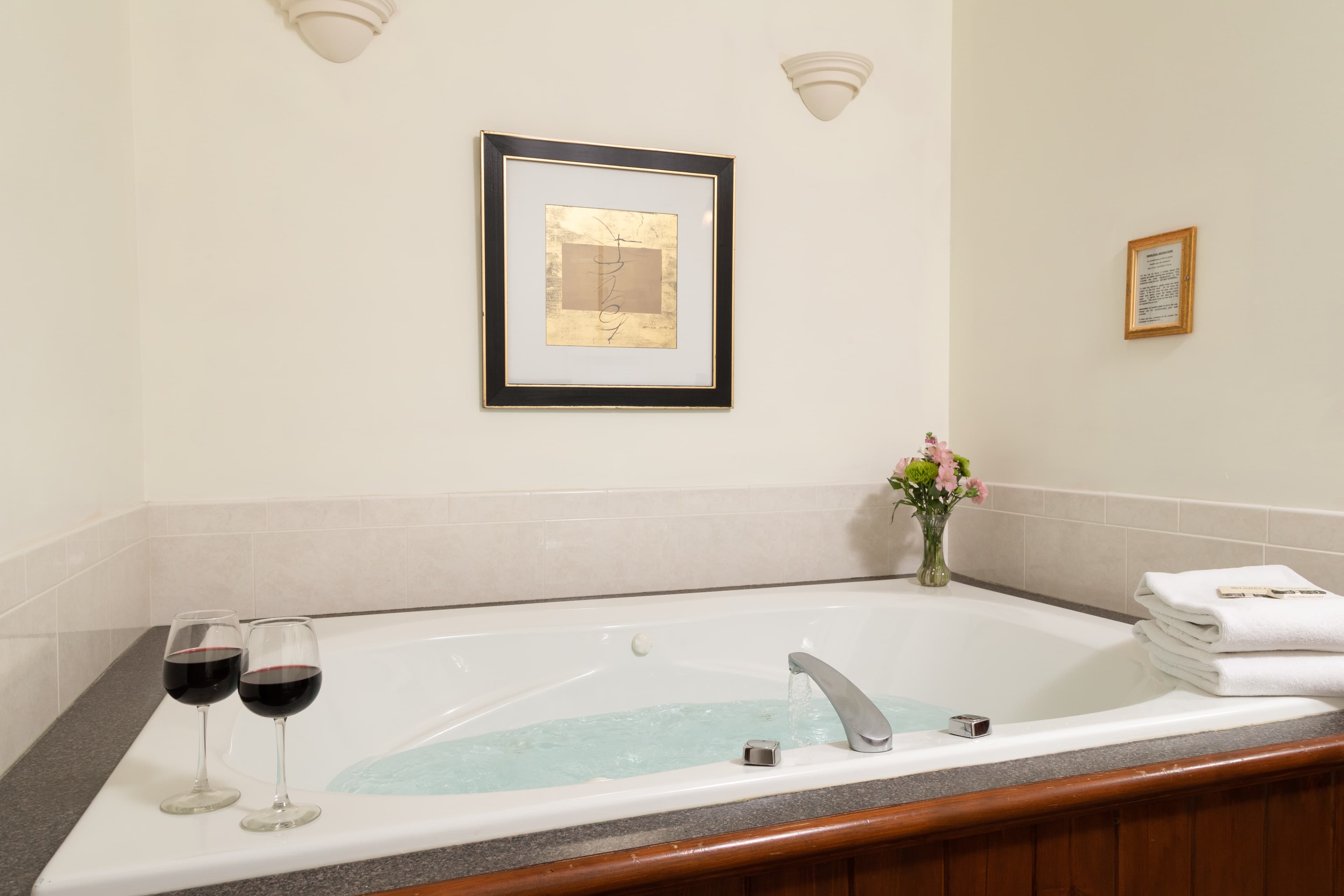 A romantic setting with a large jetted tub, two glasses of red wine, fresh flowers, and soft towels.