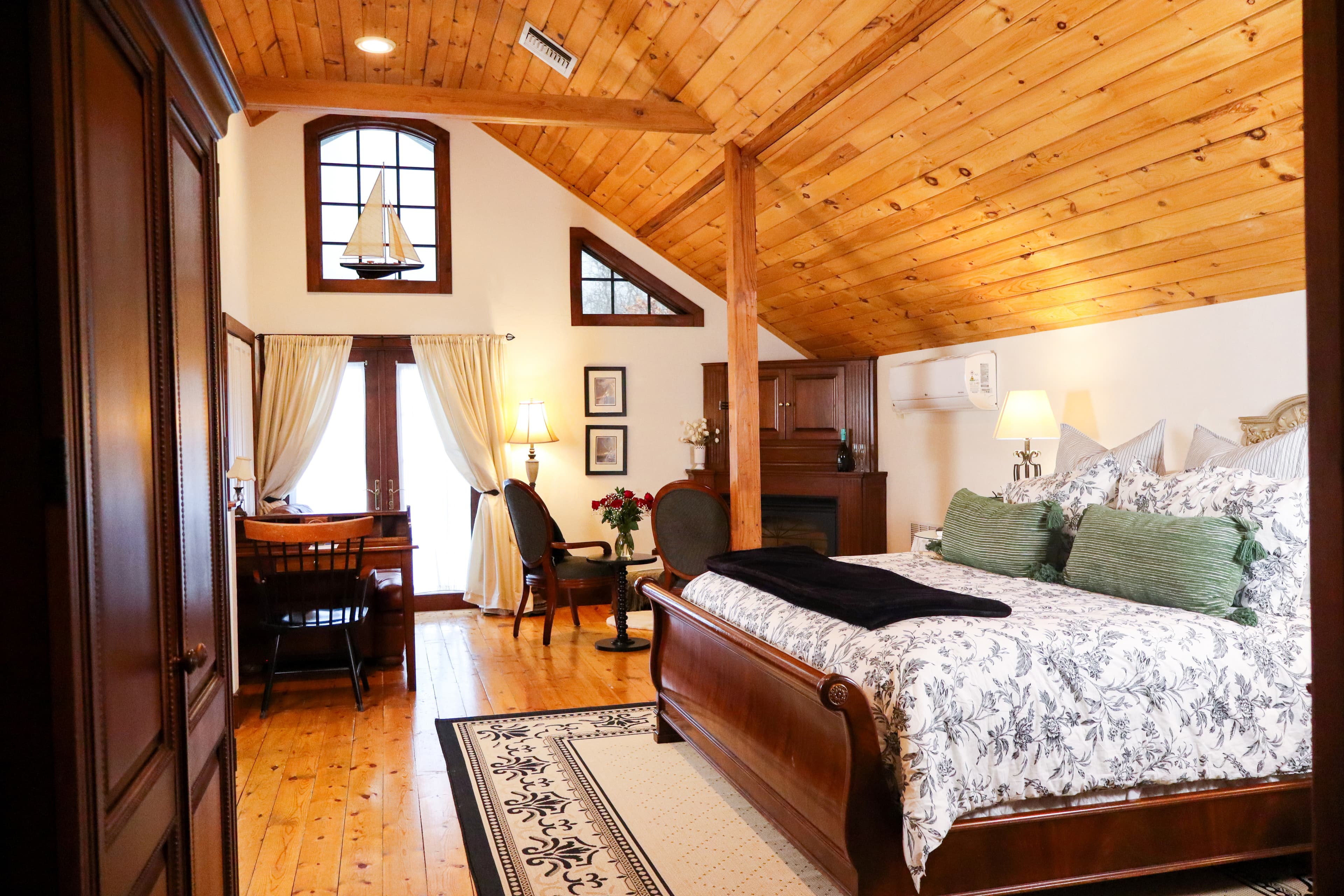 A spacious bedroom featuring a warm wood cathedral ceiling, polished hardwood floors, California king bed, and a writing desk.
