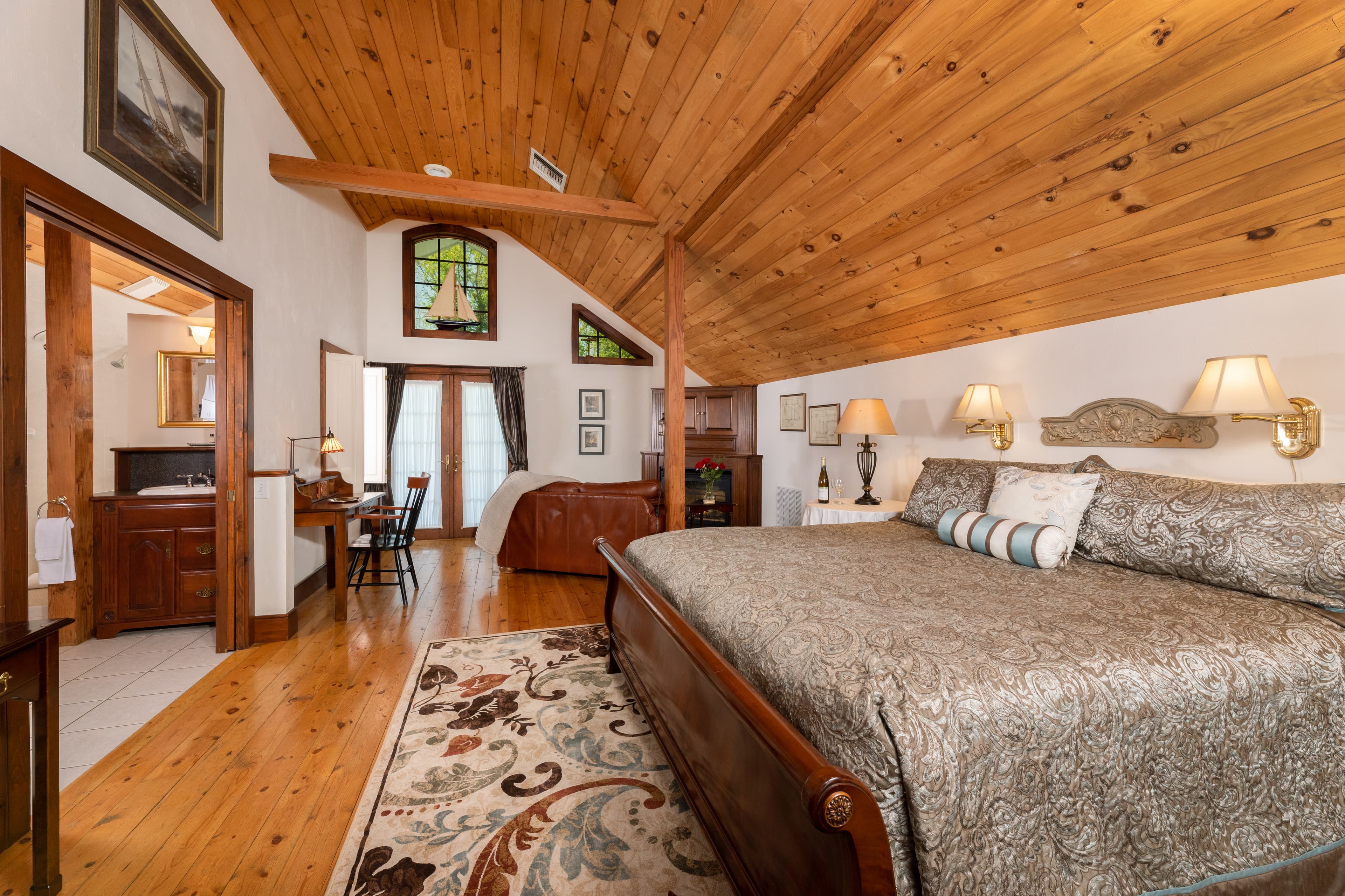 A spacious bedroom featuring a warm wood cathedral ceiling, polished hardwood floors, California king bed, and a writing desk.