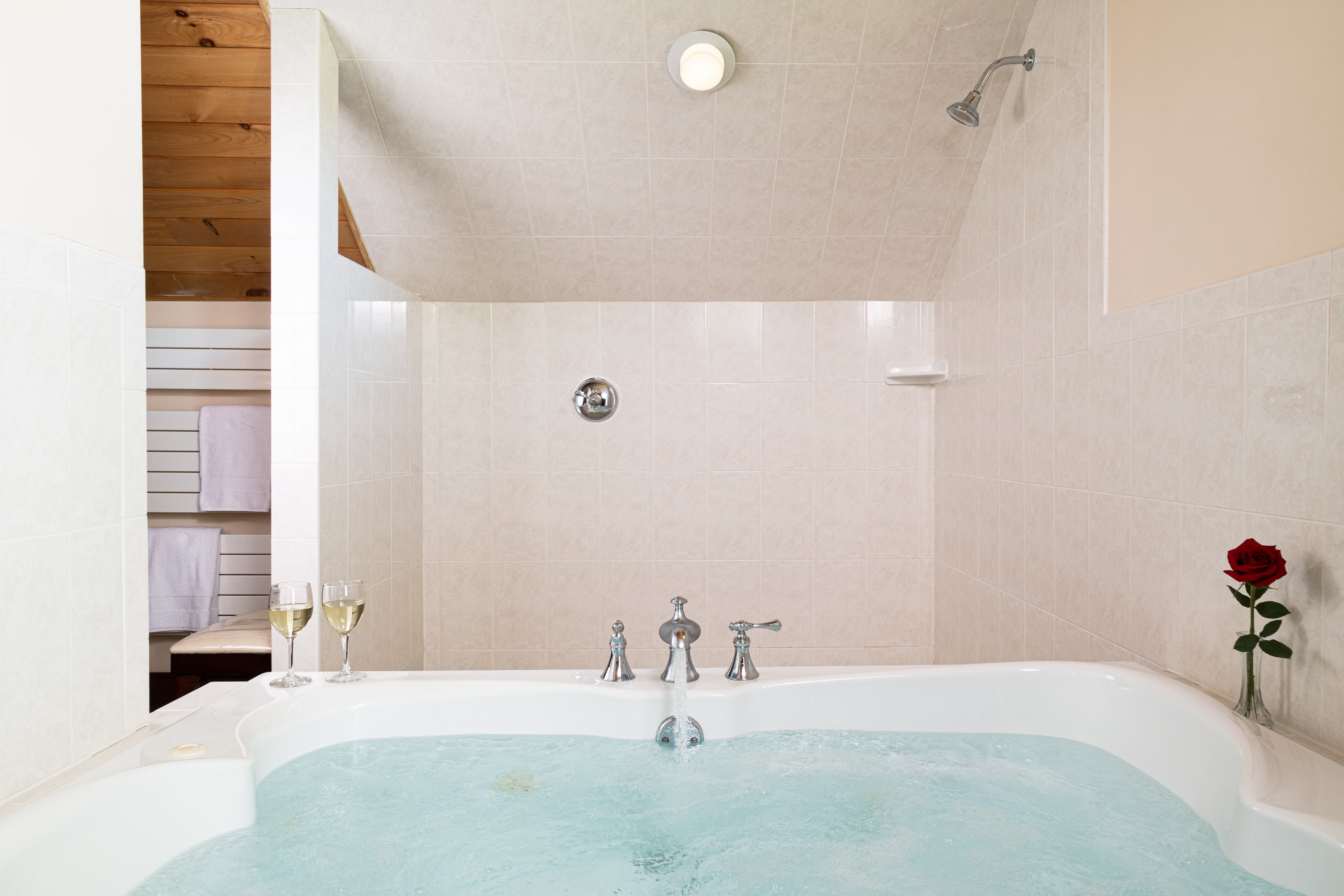 A clean, bright bathroom with a jetted soaking tub, a single red rose, and two flutes of champagne, creating a relaxing, romantic atmosphere.