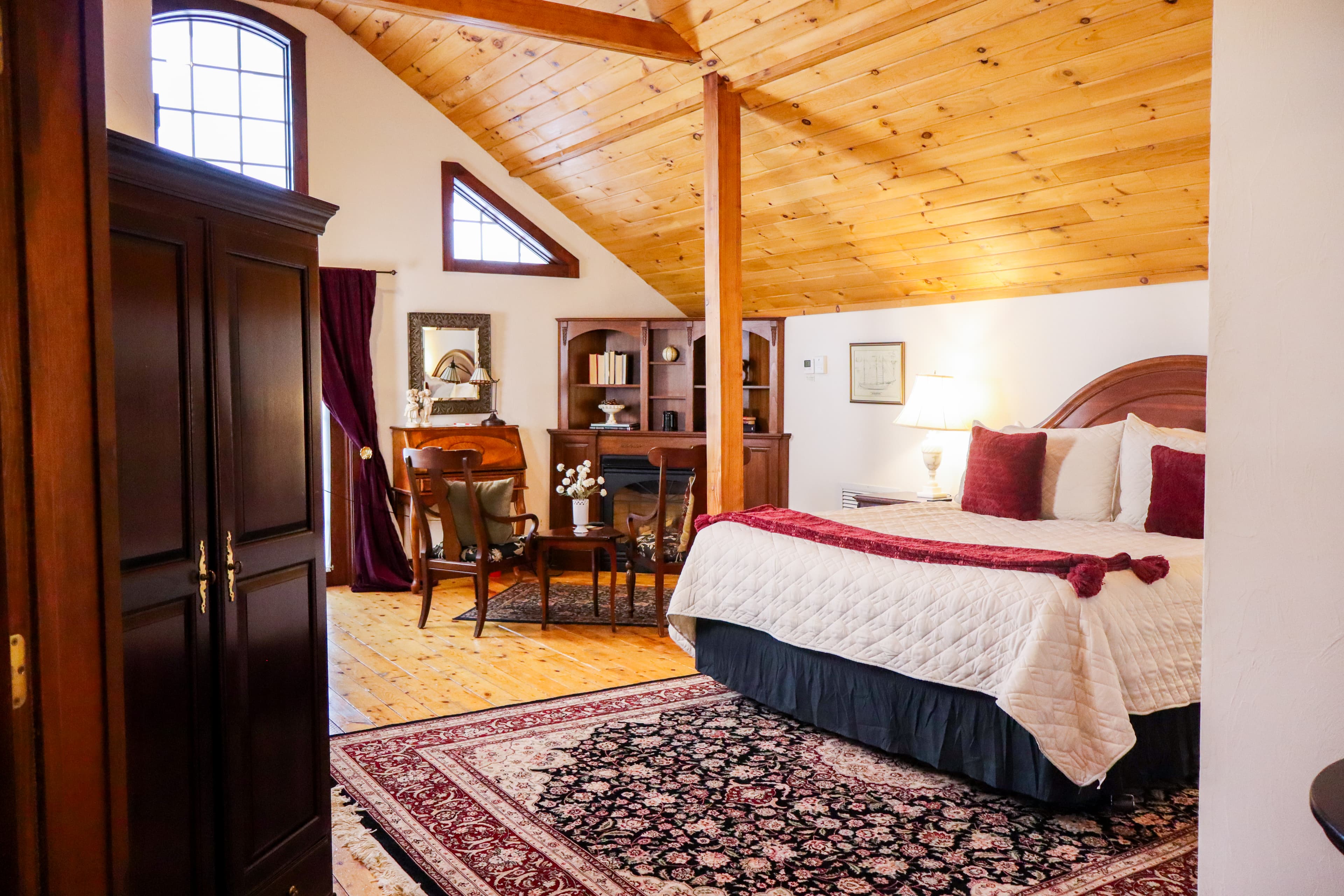 A spacious bedroom with a warm wood cathedral ceiling, hardwood floors, a king bed, and a cozy sitting area by the French doors.