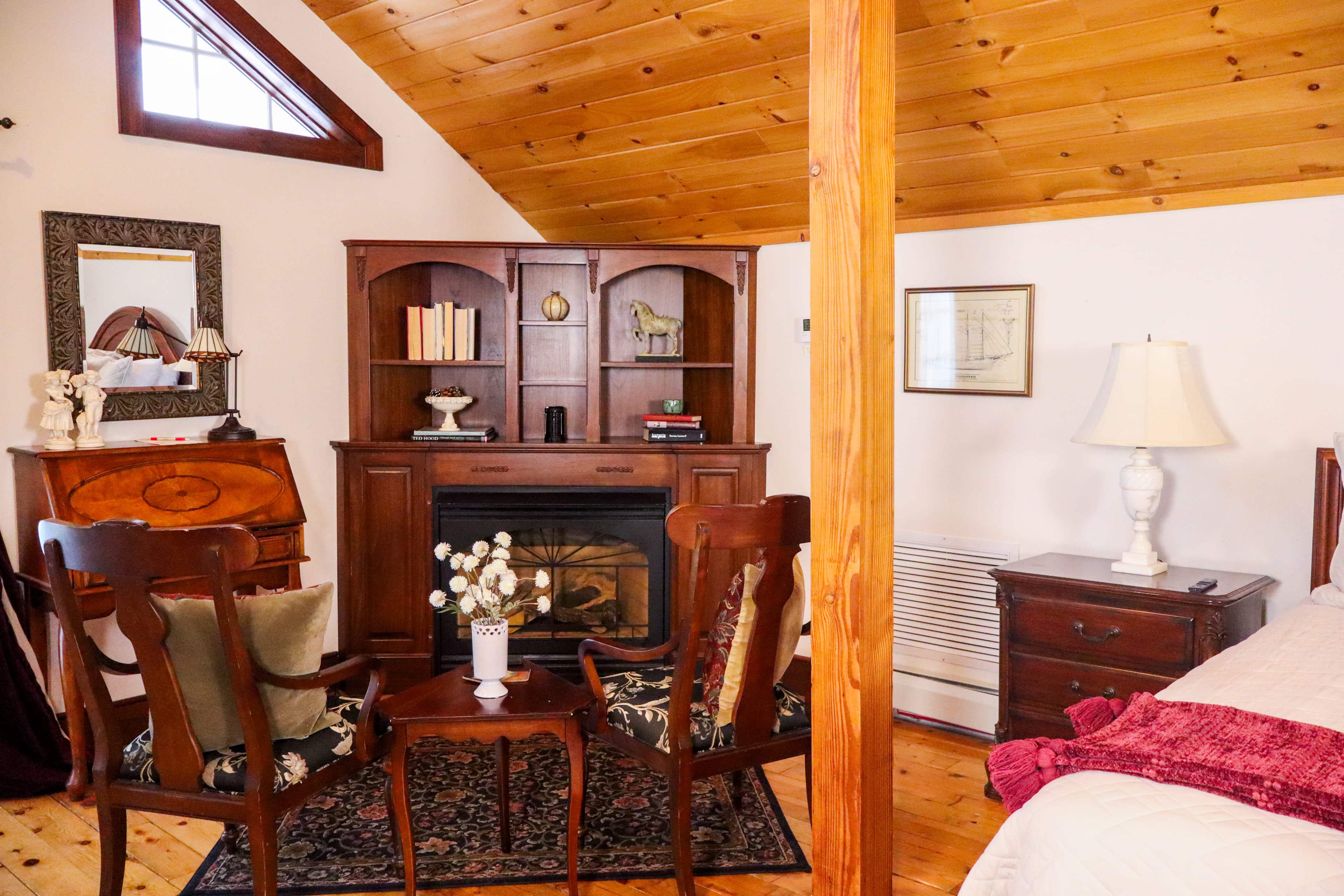 A cozy sitting area with a lit fireplace set in a dark wood bookcase mantel, flanked by two upholstered wingback chairs and an ottoman.