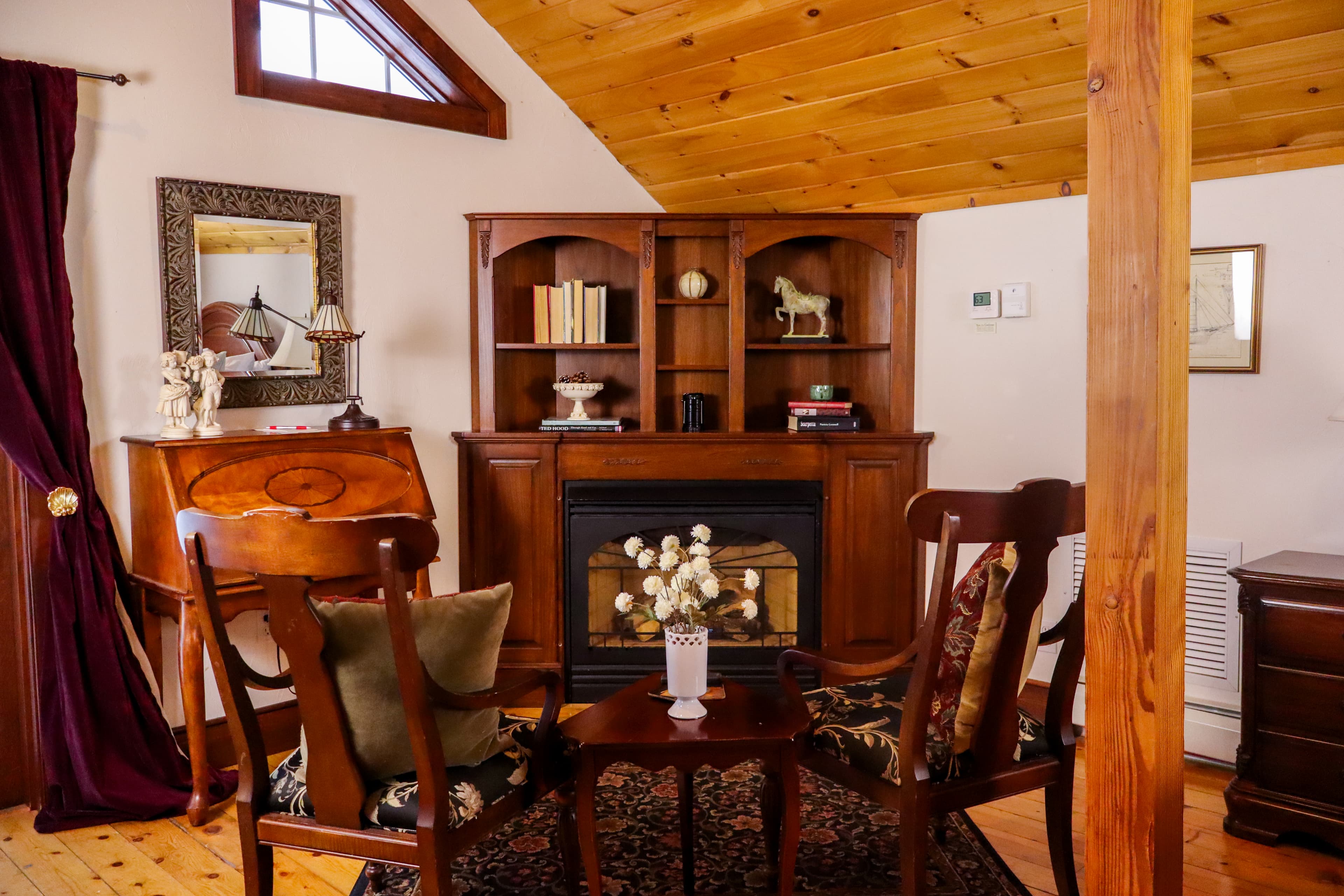 Bright French doors open to a private balcony with a small bistro table, offering a sunny view of a charming yellow building and trees.
