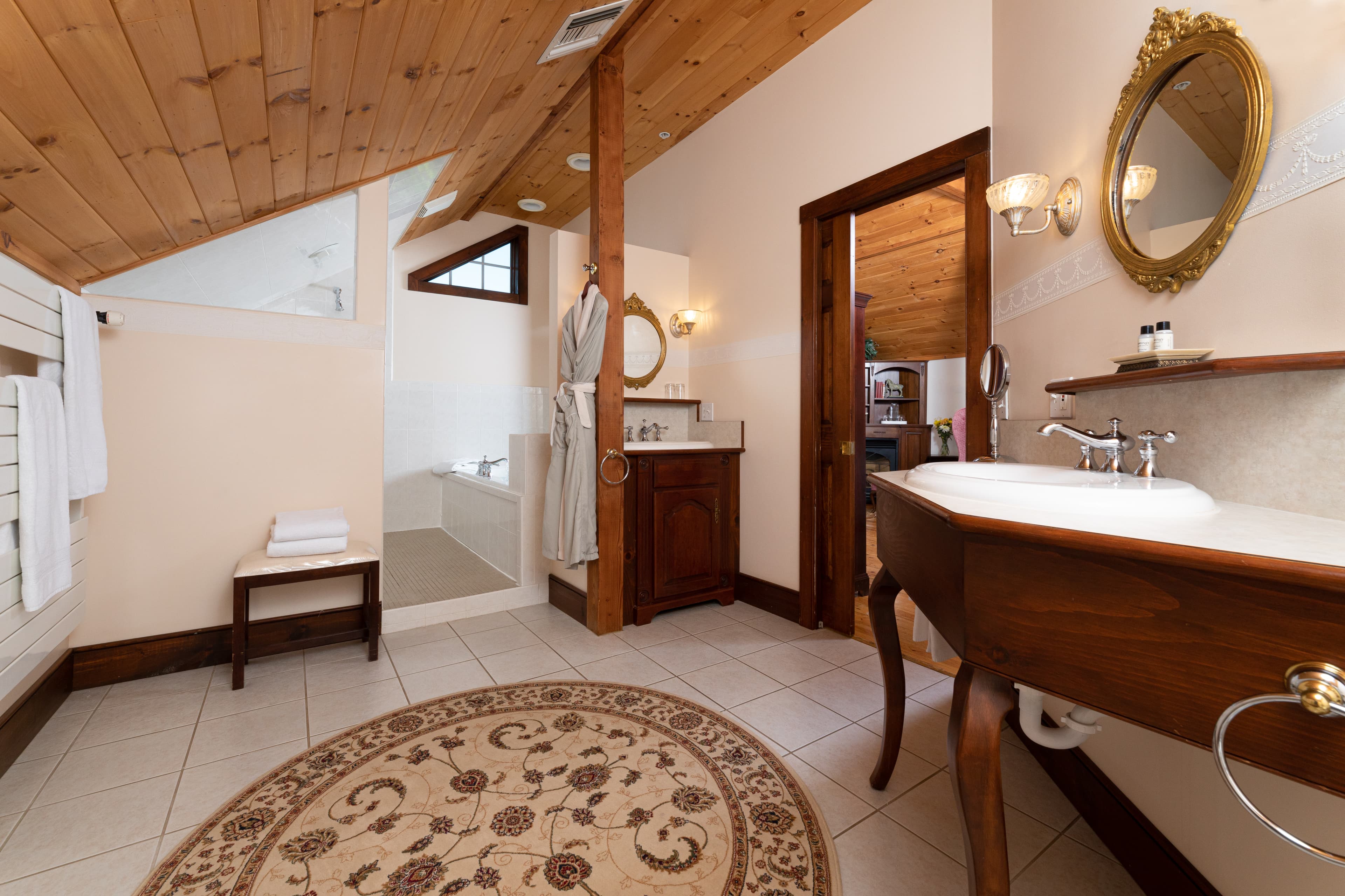 A bright, spacious bathroom with a wood-planked ceiling, a dark wood vanity, and an ornate gold-framed mirror.