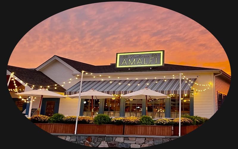 Cozy restaurant facade with "Amalfi" sign, lit by string lights against a sunset backdrop.