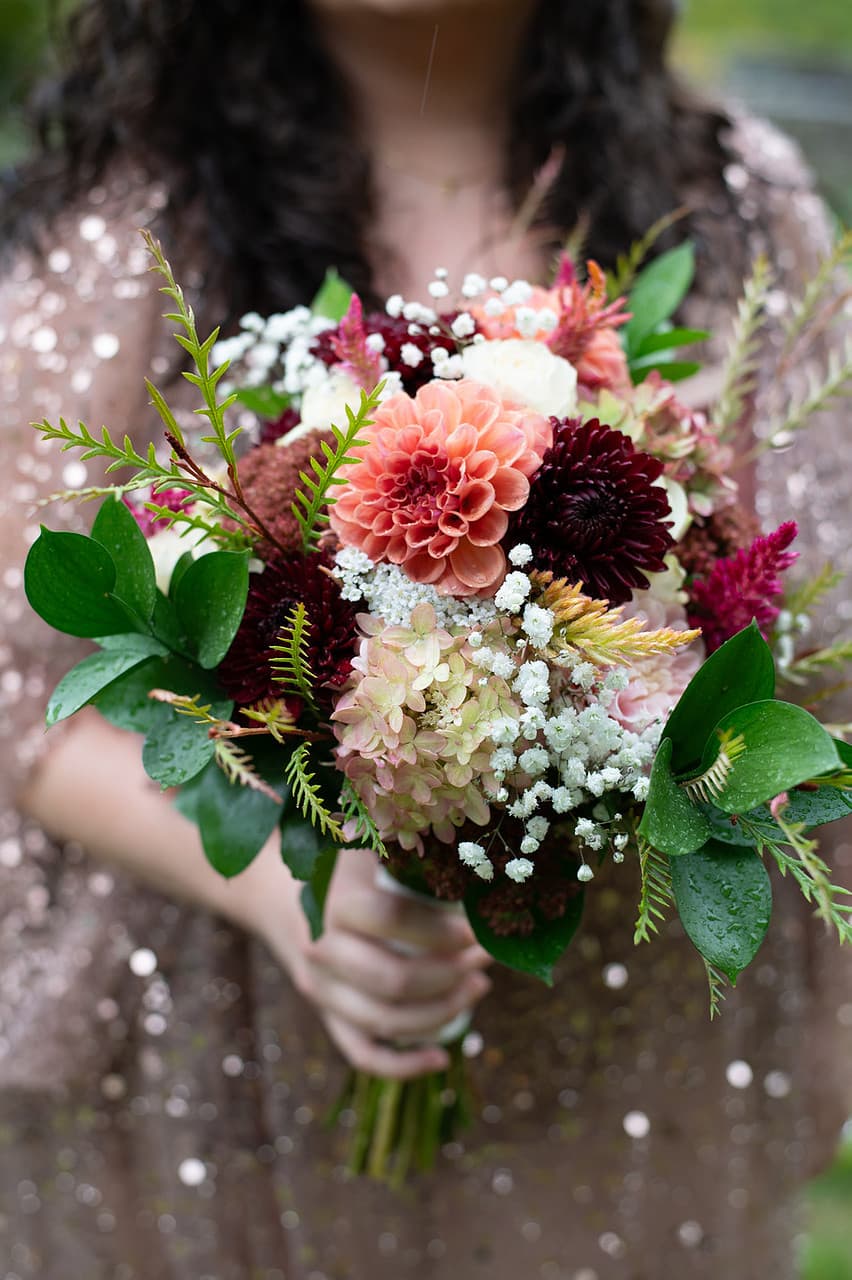A person holds a vibrant floral bouquet featuring pink, maroon, and white flowers with greenery.