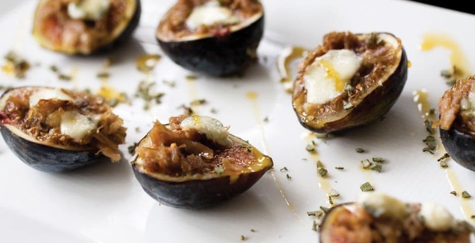 A platter of stuffed figs topped with cheese and garnished with herbs.