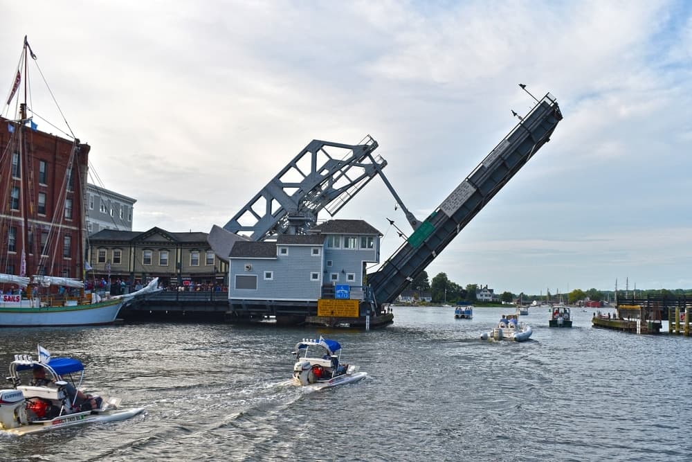 A drawbridge is being raised above a river while boats pass beneath it. A drawbridge is being raised above a river while boats pass beneath it.