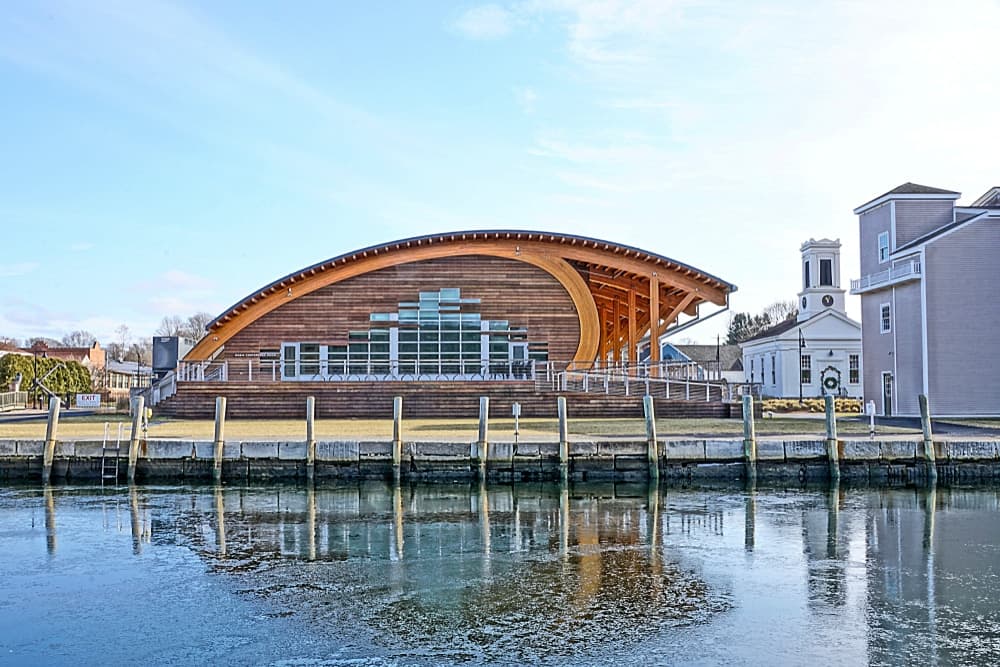 A modern wooden building with a curved roof stands beside a calm waterway.