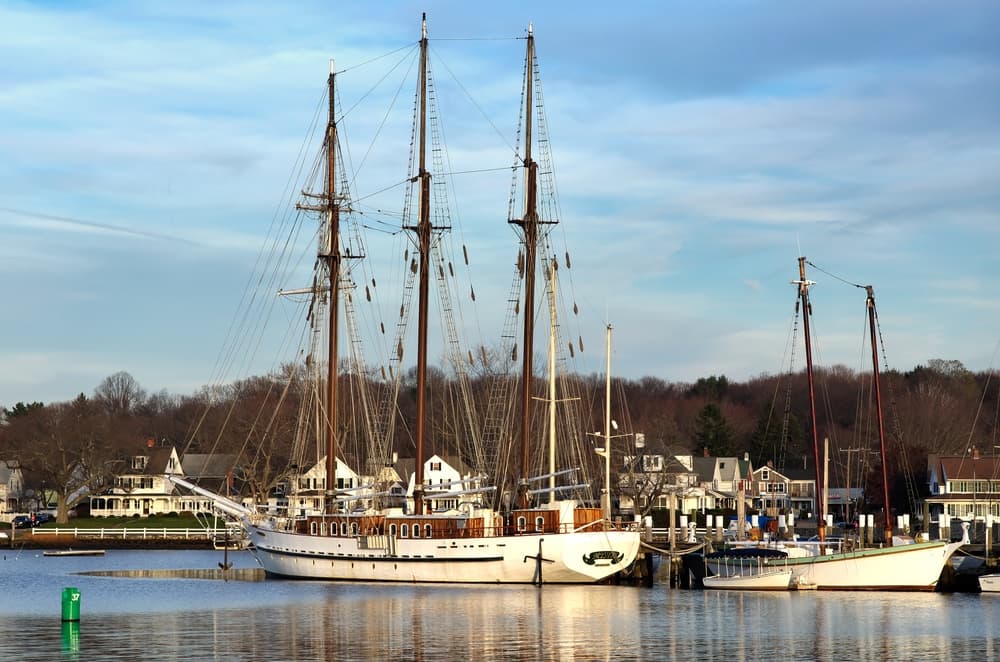 A tall ship docked at a marina surrounded by waterfront homes and trees.