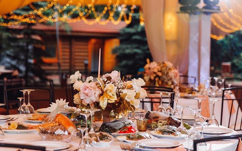 A beautifully arranged dining table with a floral centerpiece and an array of dishes, set under twinkling lights.