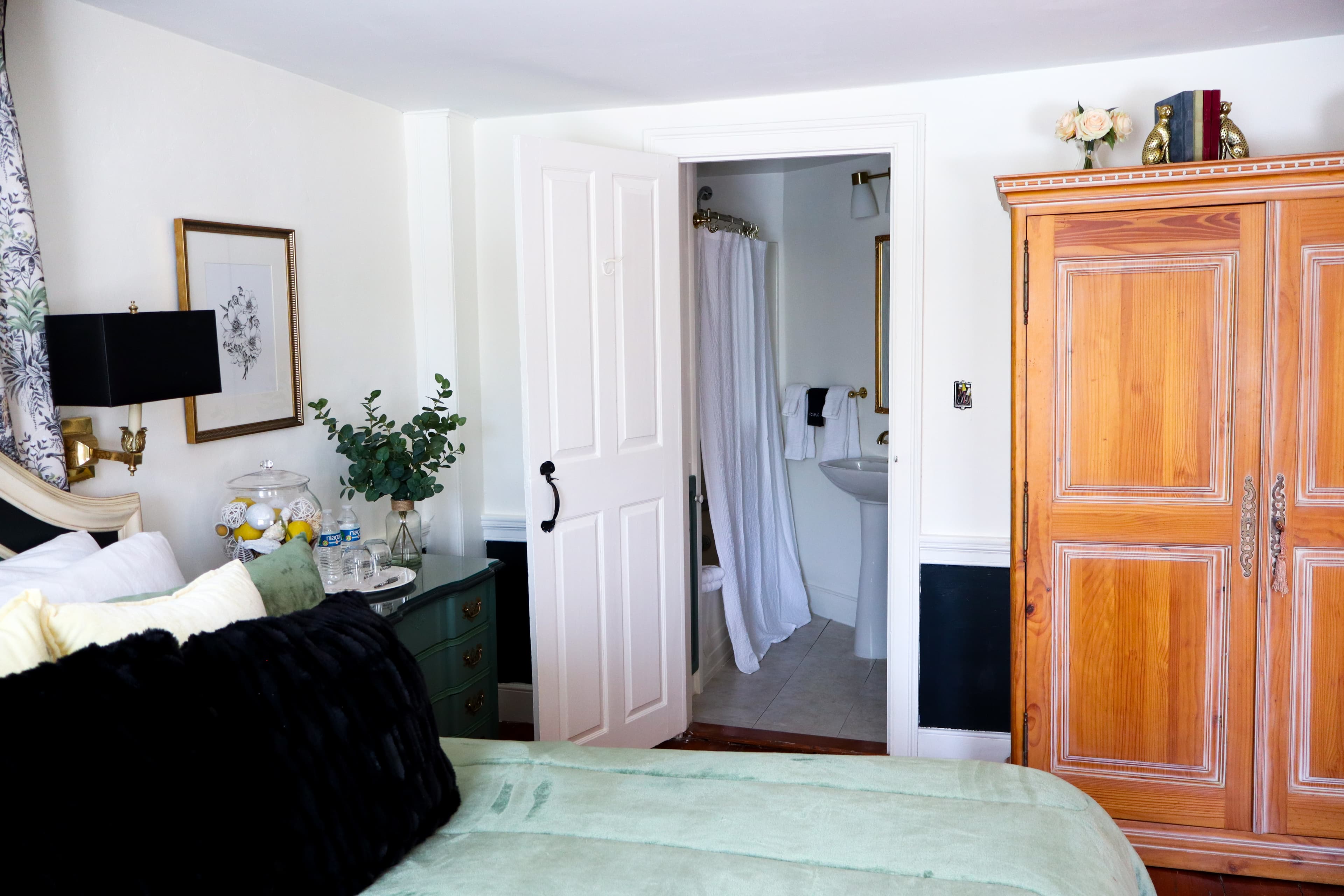 A cozy bedroom featuring a green bedspread, an open bathroom door, and wooden furniture.