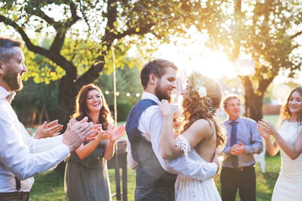 A joyful couple dances together during their outdoor wedding celebration, surrounded by smiling guests.