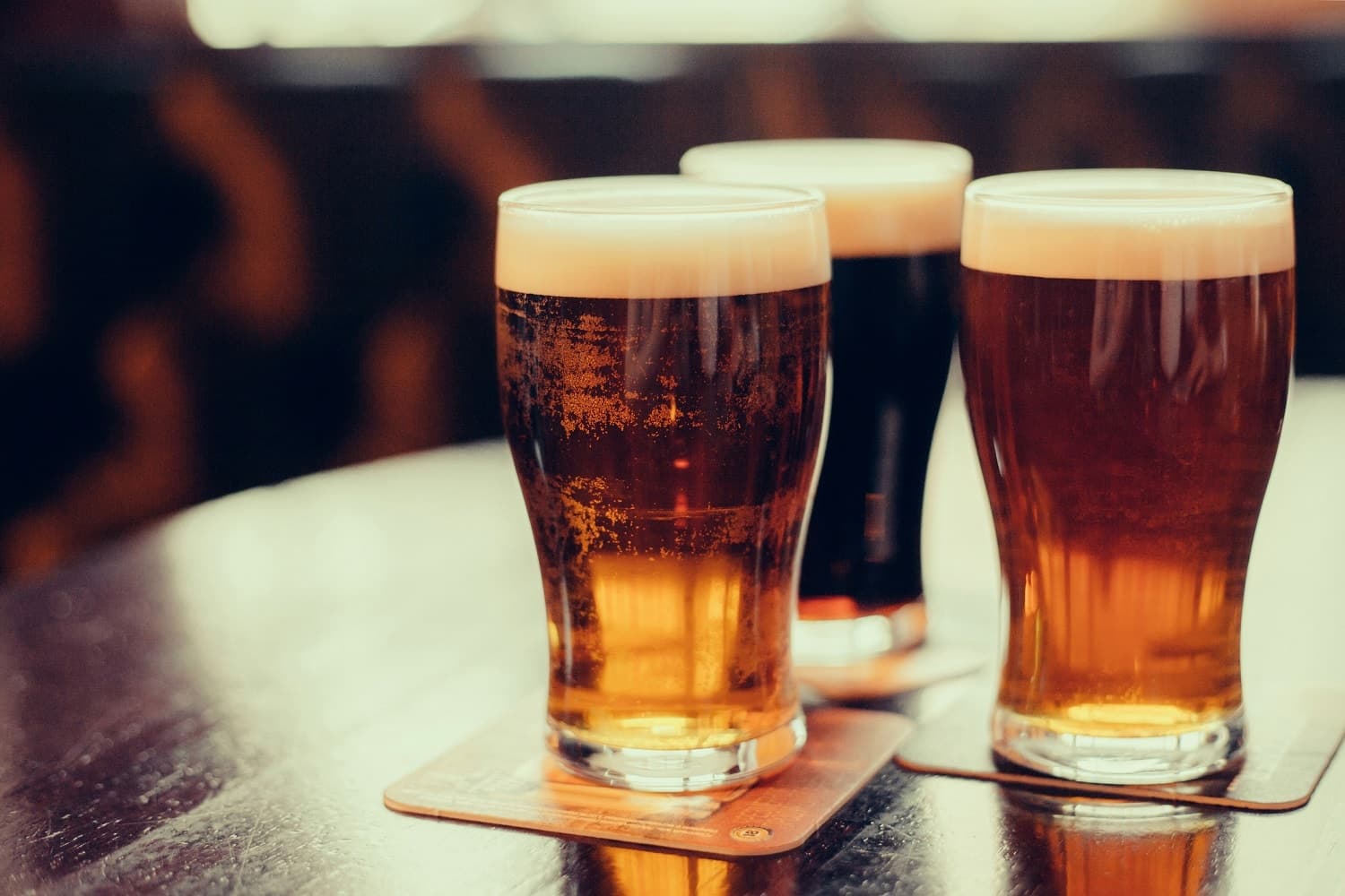 Three glasses of beer with varying colors and foamy tops on a wooden table.
