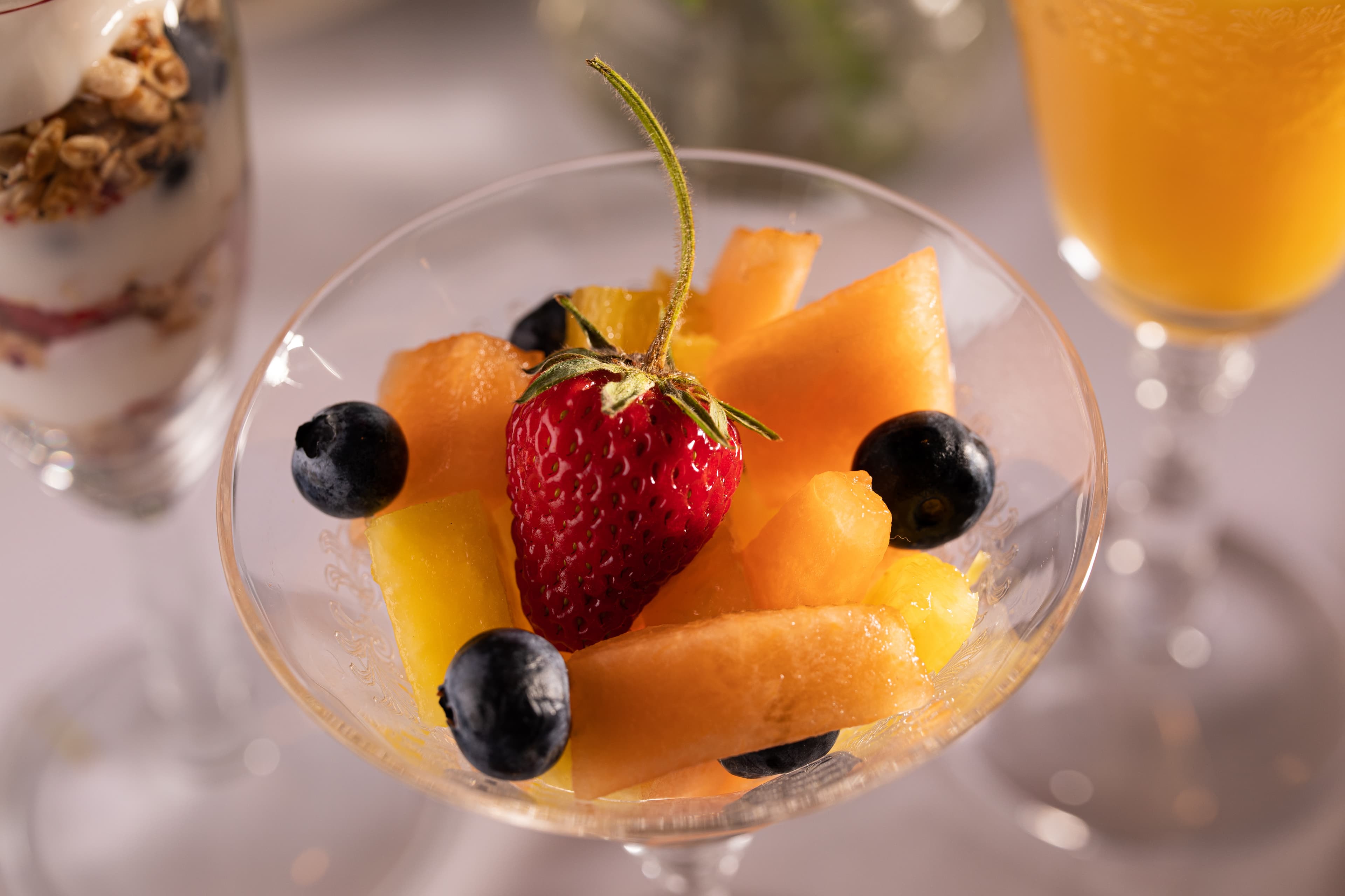 A glass dish filled with assorted fresh fruits, including chunks of cantaloupe, honeydew, and a strawberry on top.