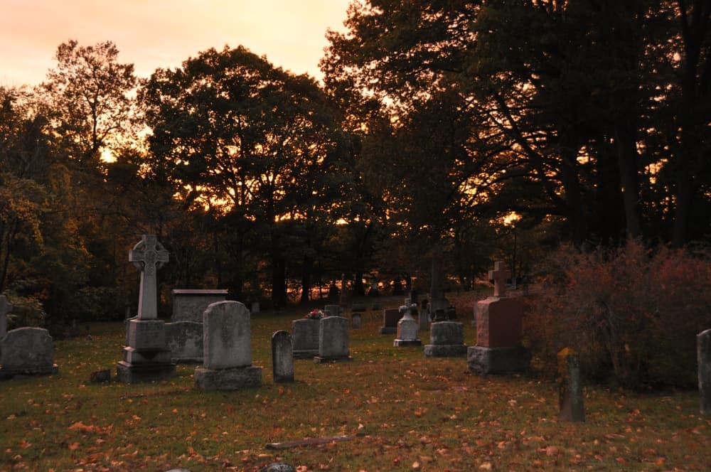 Gravestones and a cross silhouette against a vibrant sunset sky in a cemetery.