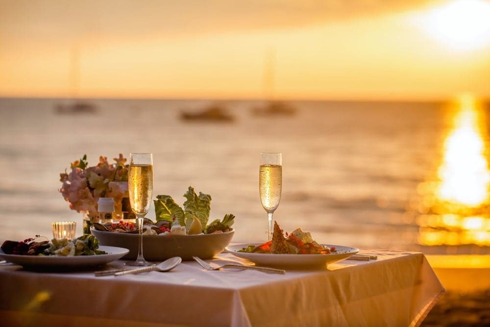 A beautifully set table with gourmet dishes and champagne flutes at sunset by the ocean.