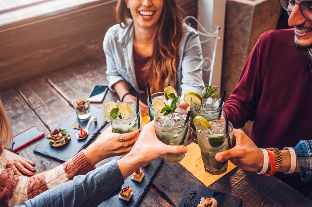 A group of friends cheers with cocktails while enjoying appetizers at a table.
