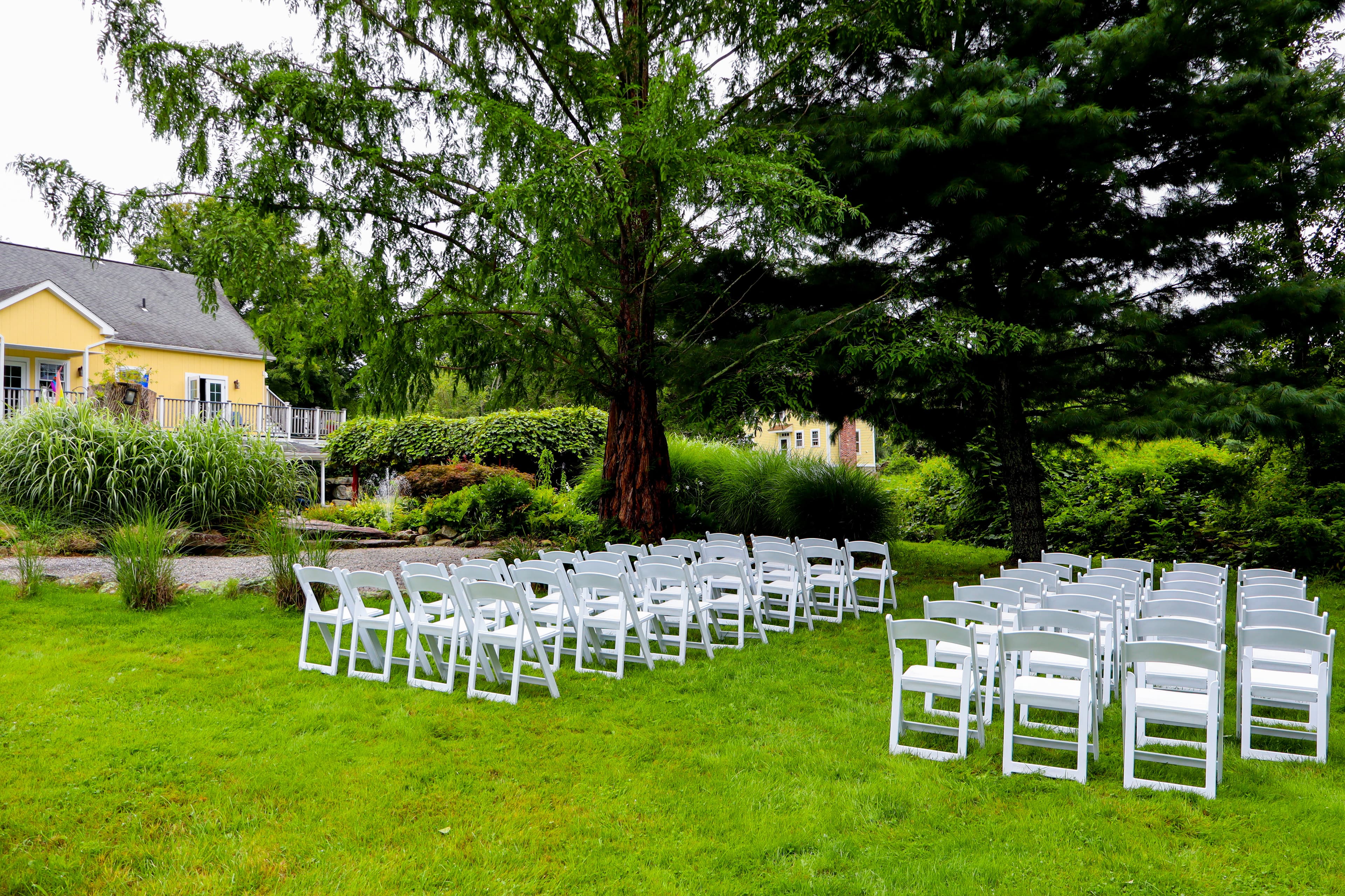 A landscaped outdoor area with white folding chairs arranged for an event.