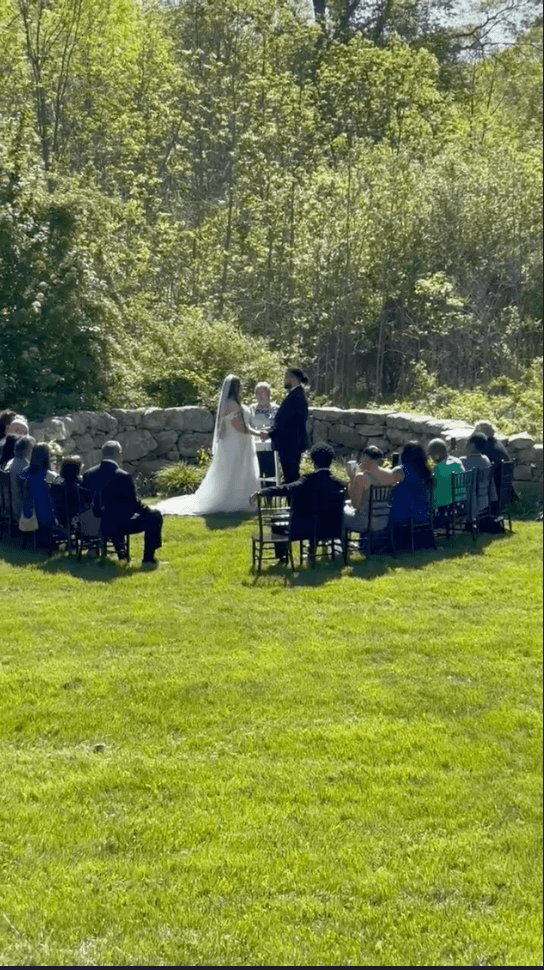 A couple exchanges vows during an outdoor wedding ceremony surrounded by guests.
