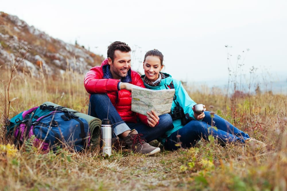 A couple sitting in a grassy field, examining a map while enjoying the outdoors.