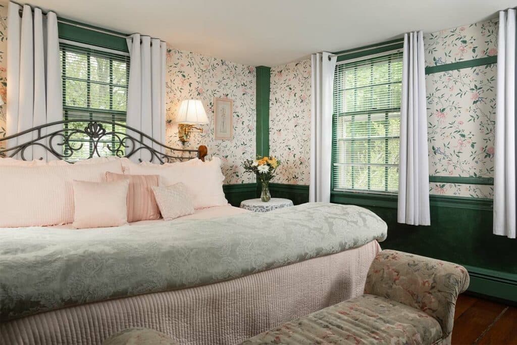 Cozy bedroom featuring floral wallpaper, a large bed with soft linens, a lamp, and a small table with a flower vase.
