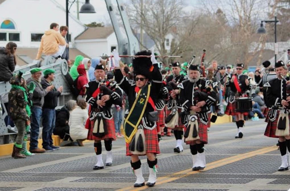 A parade featuring men in traditional Scottish attire playing bagpipes, with spectators watching from the sidelines.