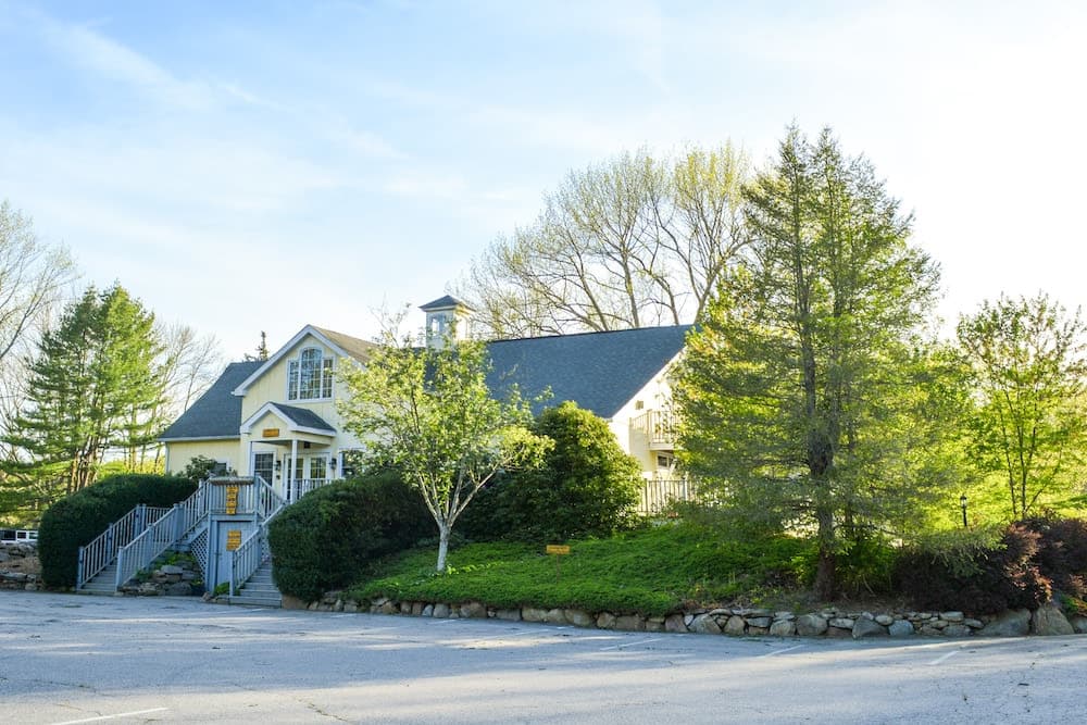 A charming two-story house surrounded by greenery and trees on a sunny day.