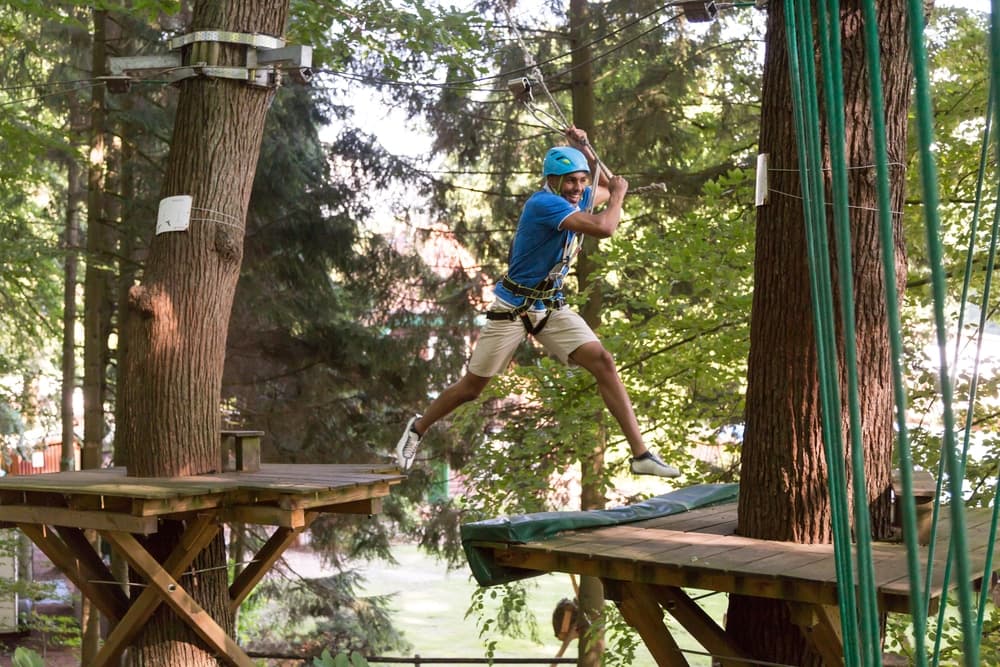 A man zips between treetops on a zip line in a forested setting.