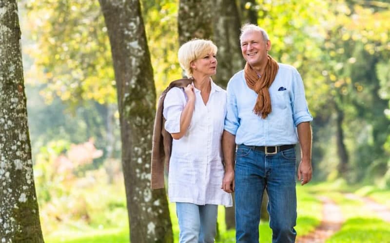 A happy couple walks hand-in-hand on a tree-lined path.