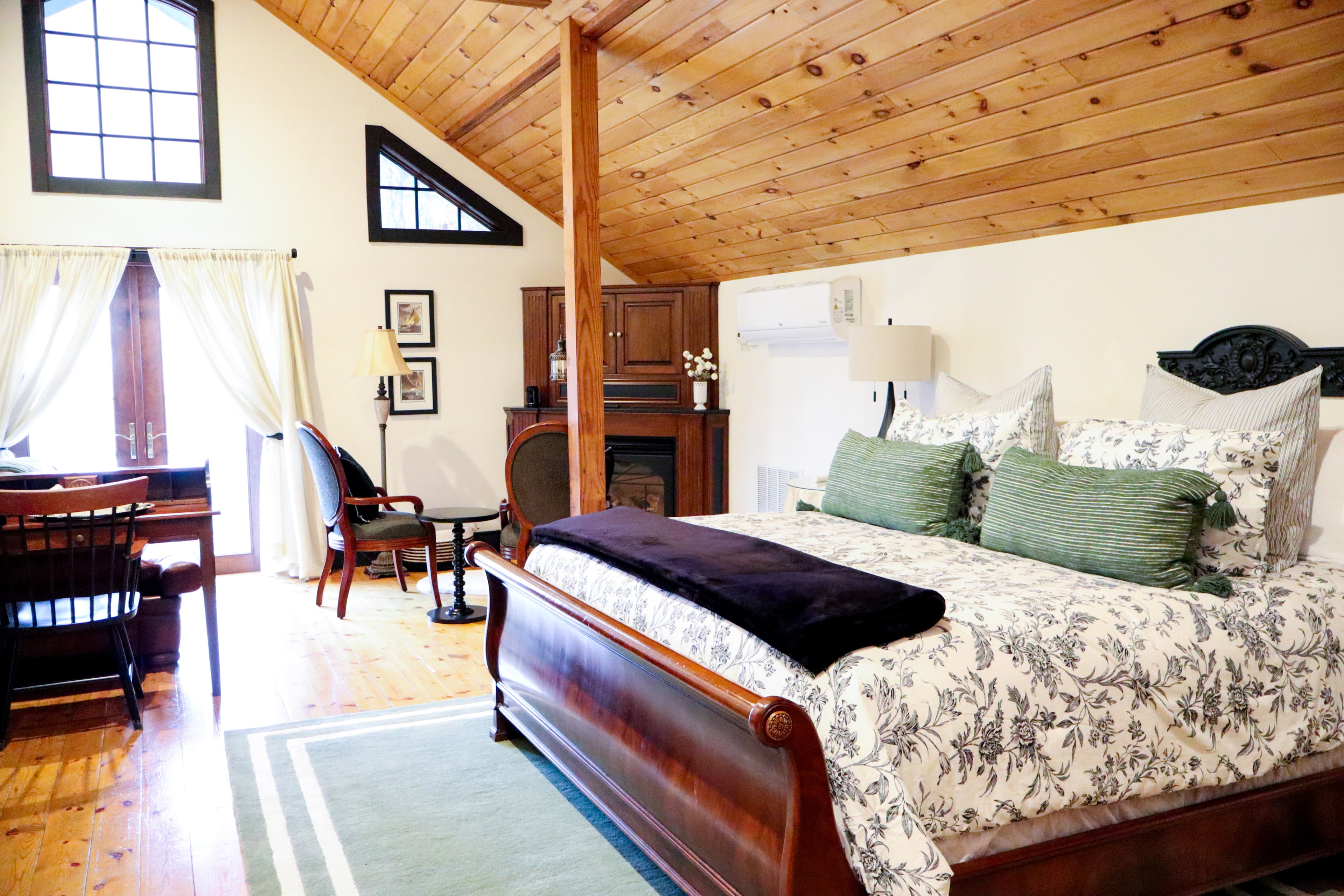 A cozy bedroom featuring a wooden sleigh bed, floral bedding, and a rustic ceiling with wooden beams.
