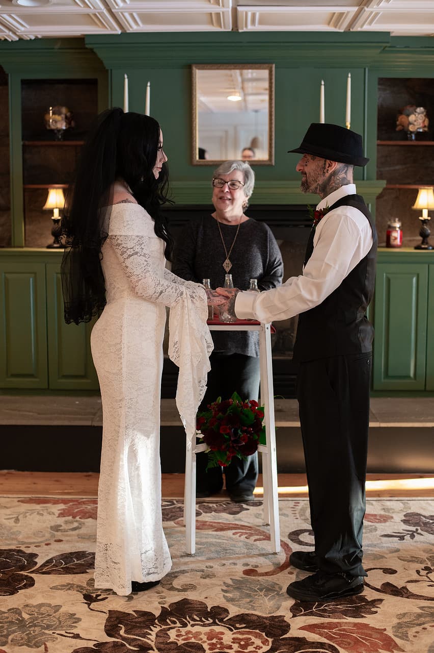A couple in formal attire exchanges vows during a wedding ceremony, with an officiant present.
