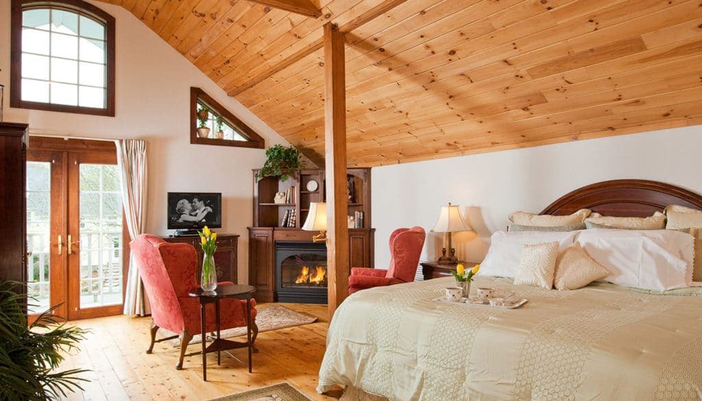 A cozy, rustic bedroom with a wooden ceiling, a fireplace, and two armchairs.