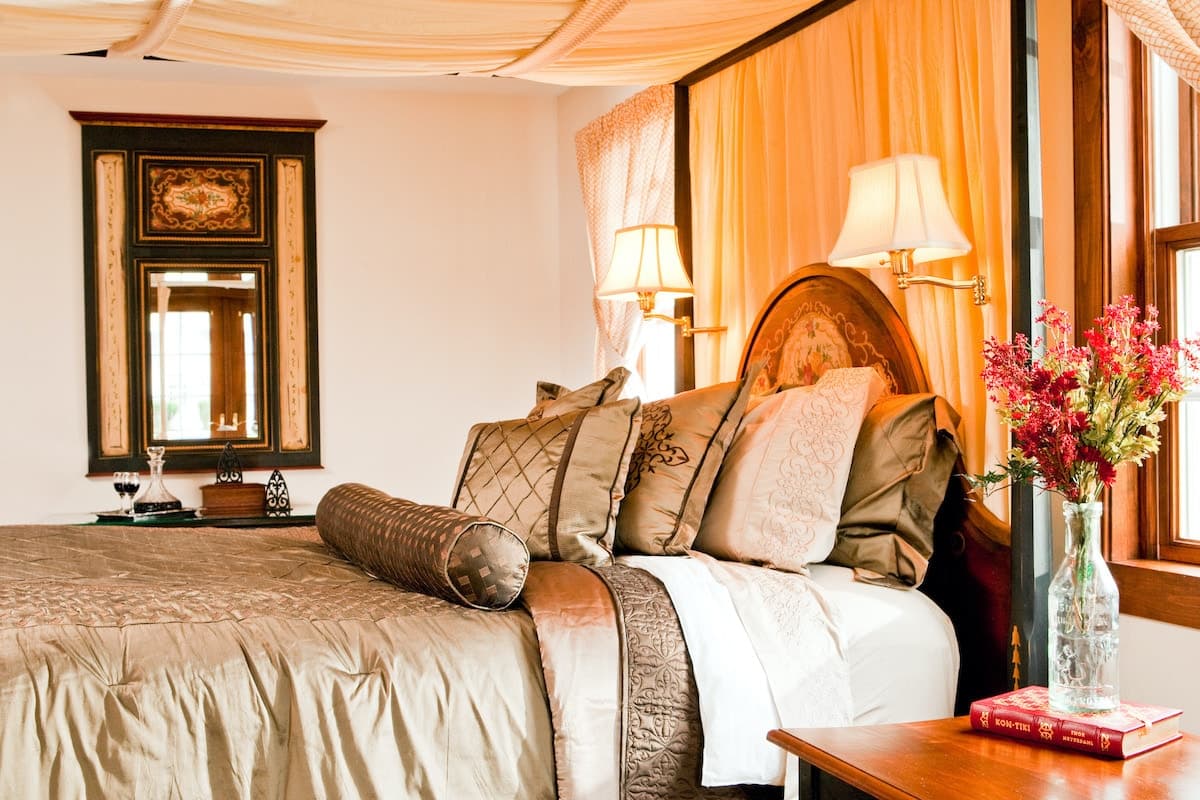 A cozy, elegantly decorated bedroom featuring a king-sized bed with rich brown and cream bedding, a mirror, and soft lighting.