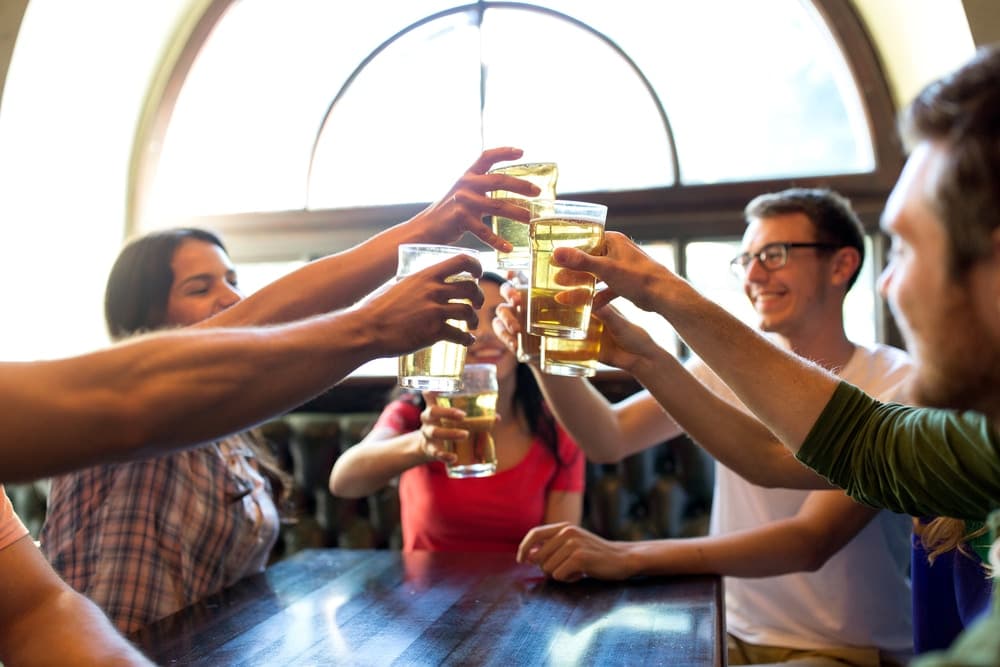 A group of friends toasting with drinks at a table in a lively setting.