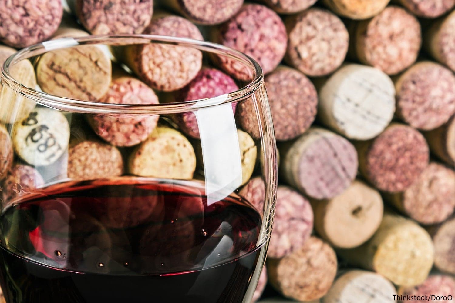 A close-up of a glass of red wine in front of a background of wine corks.
