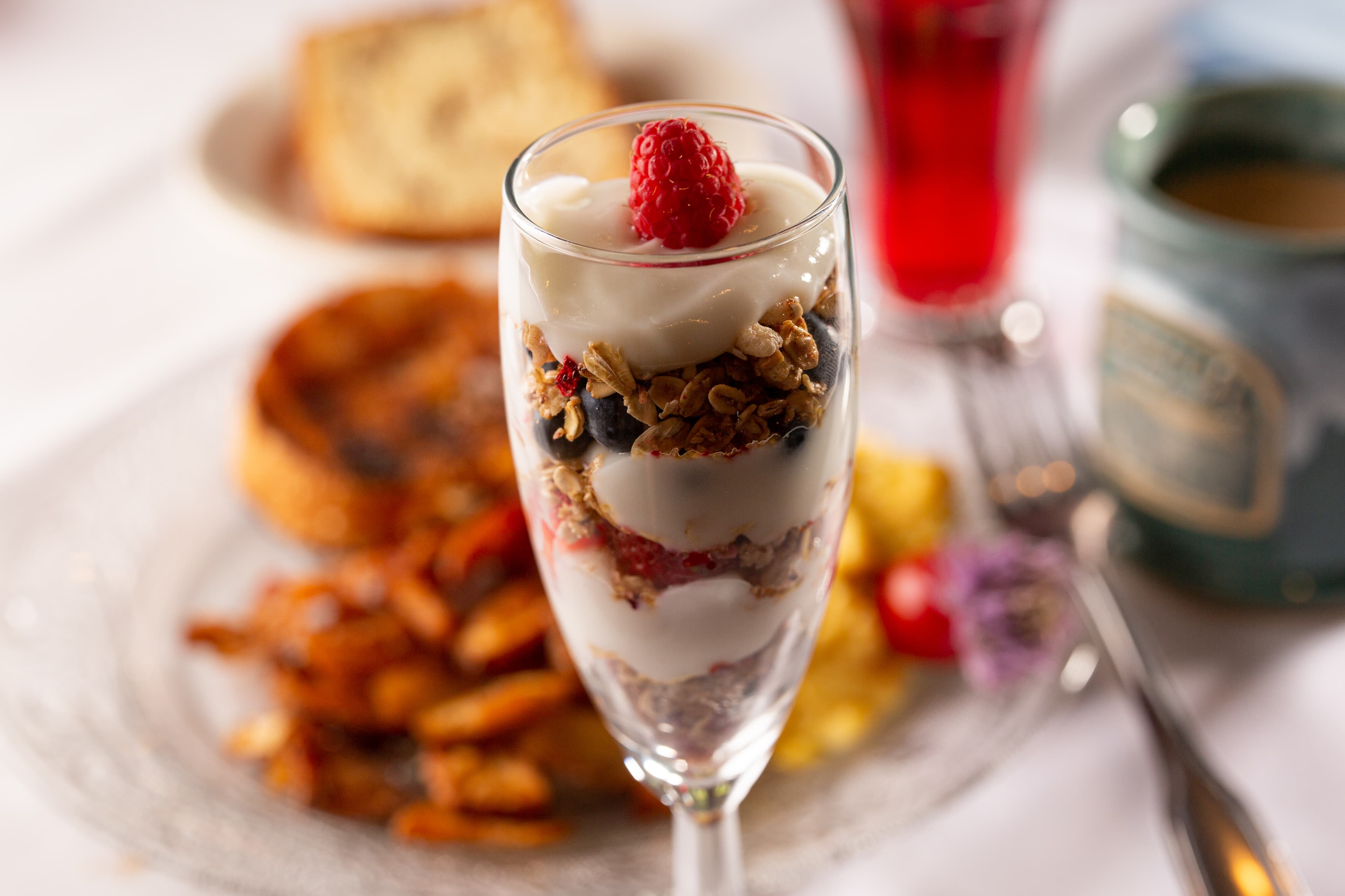A parfait glass filled with yogurt, granola, and berries, accompanied by toast and a colorful drink.