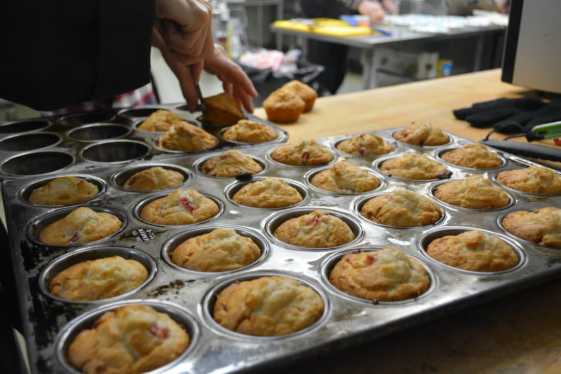A hand reaches for a freshly baked tray of muffins in a kitchen.