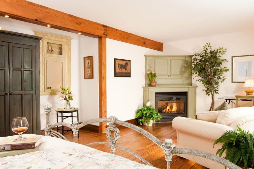 A cozy bedroom with a fireplace, wooden beams, and a comfortable sitting area.