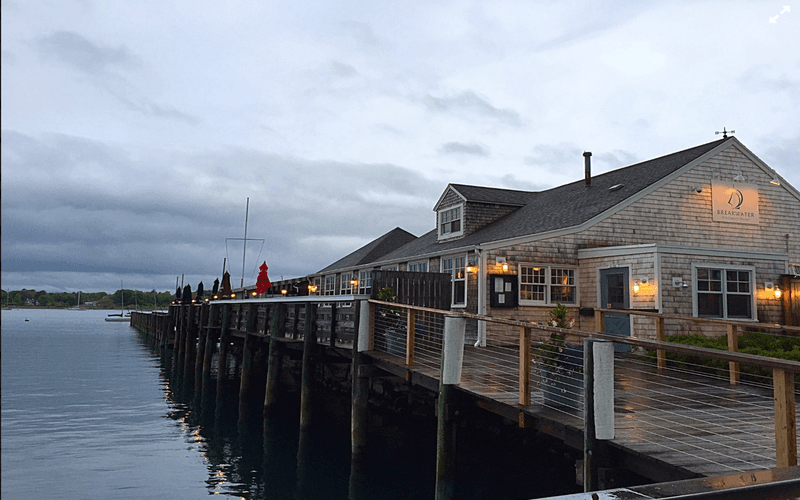 A wooden pier leads to a cozy waterfront restaurant under a cloudy sky.